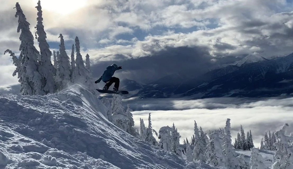 Startup TNT's Haley Jabusch going off a massive jump on her snowboard with a luxurious mountain landscape in the background.