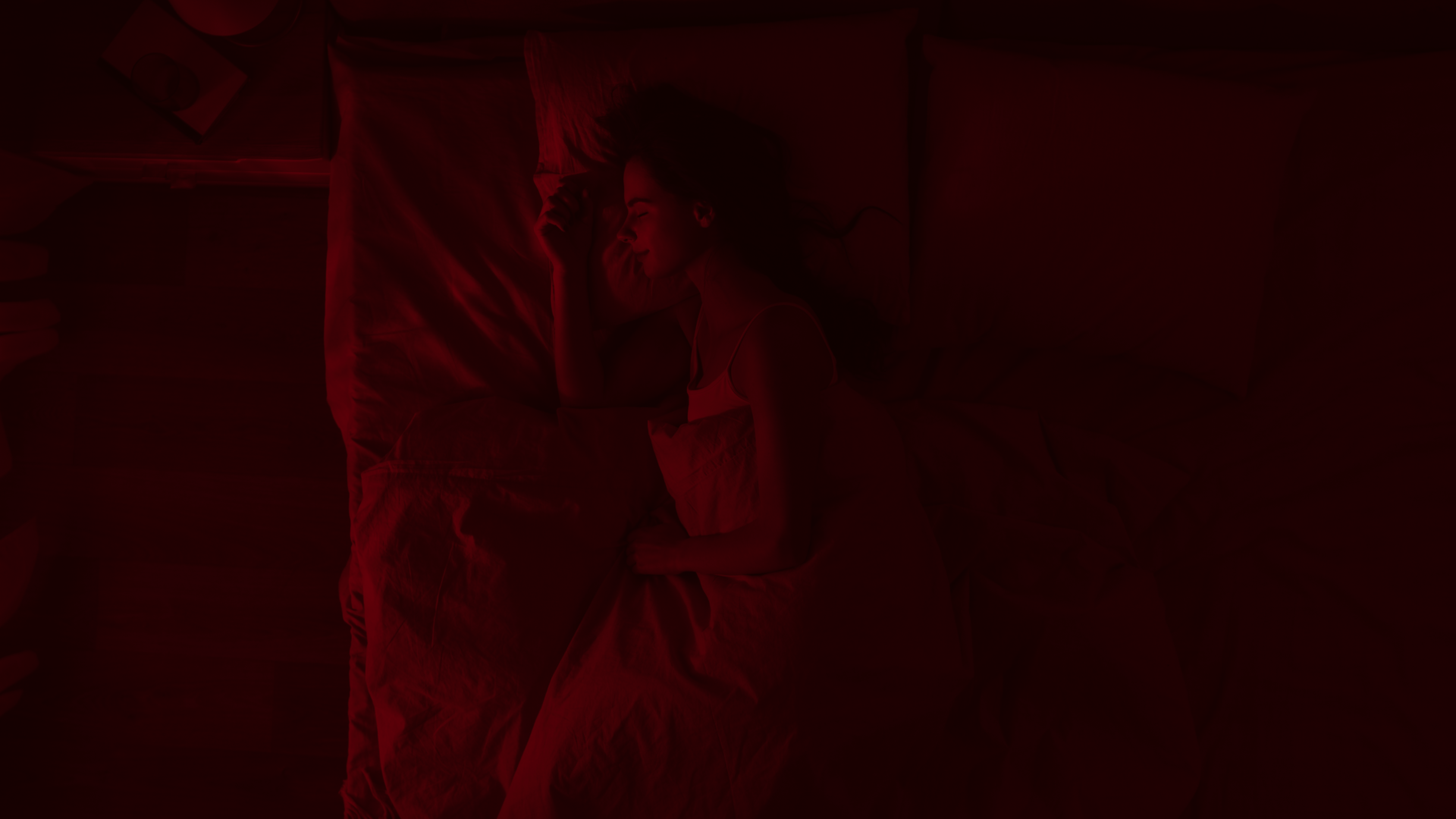 A woman sleeping on her side in bed under a dark red hue.