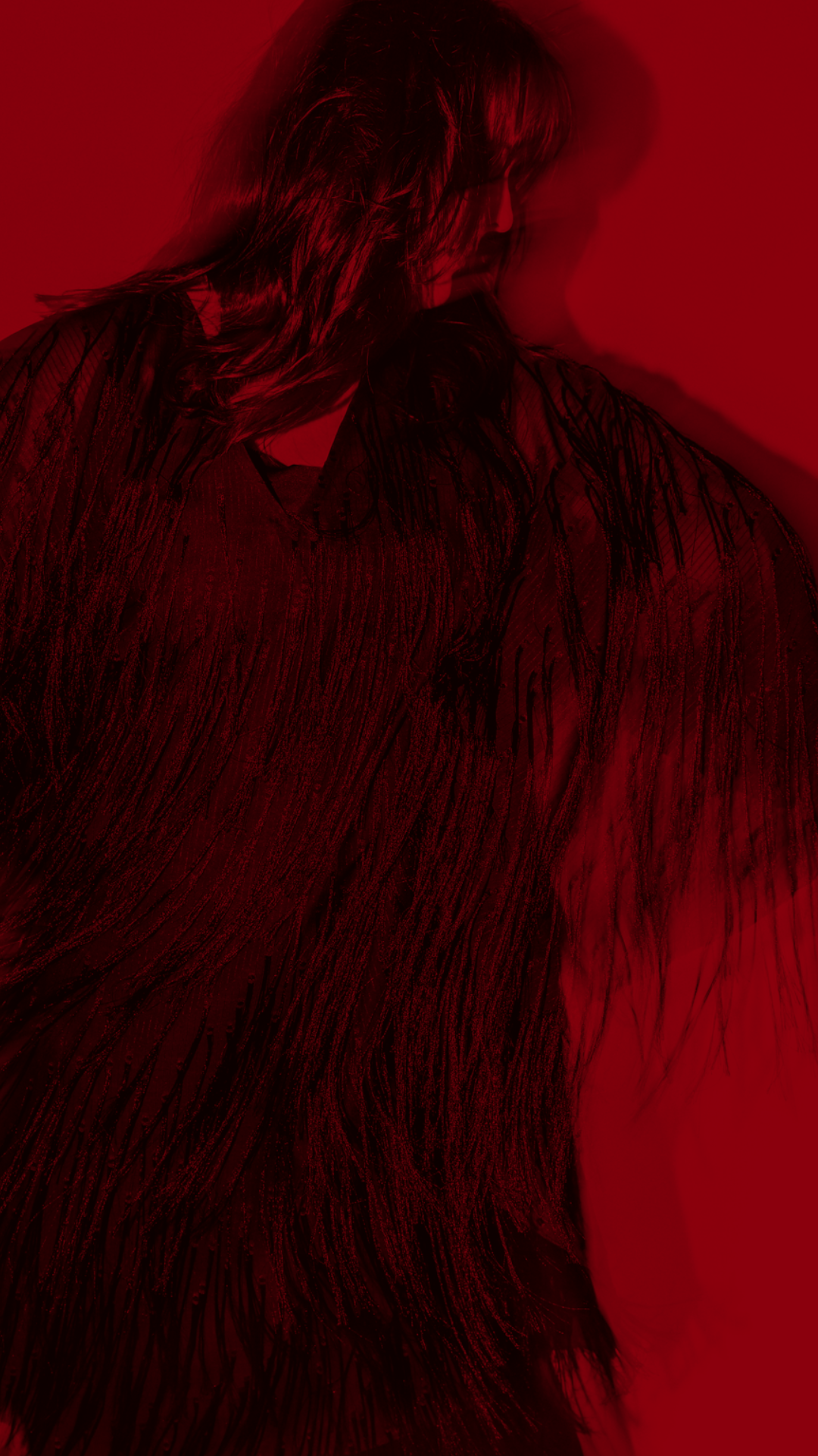 A woman with long hair wearing a flowing dark dress, illuminated by red lighting, with a blurred effect.