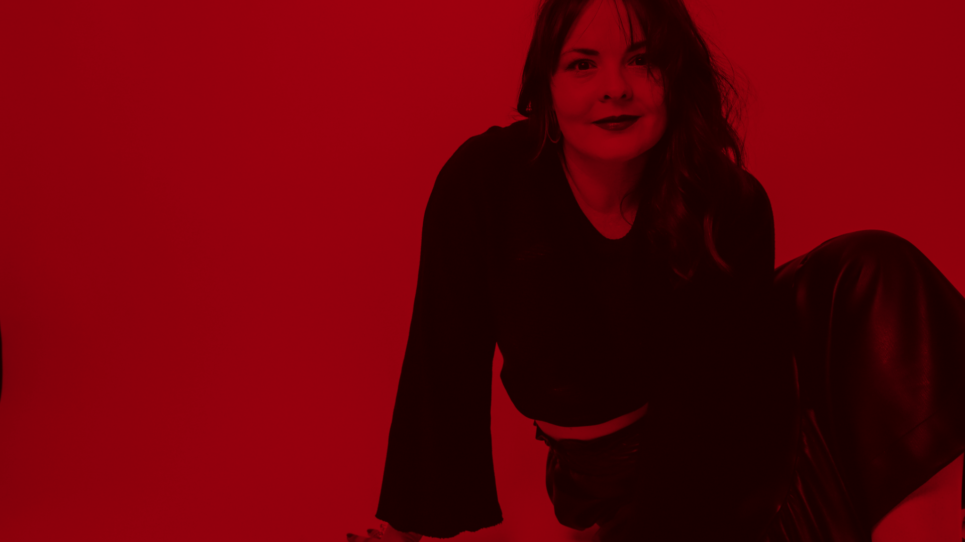 Woman in black clothing posing against a red background