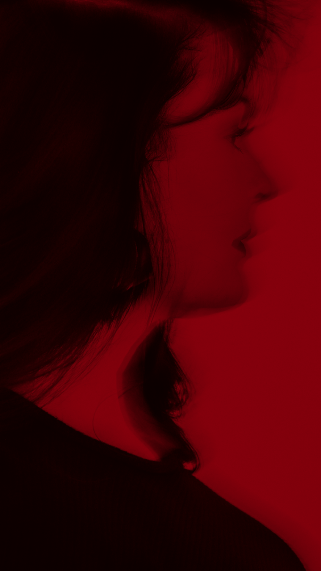 Silhouette of a person's side profile with long hair, illuminated by red lighting.