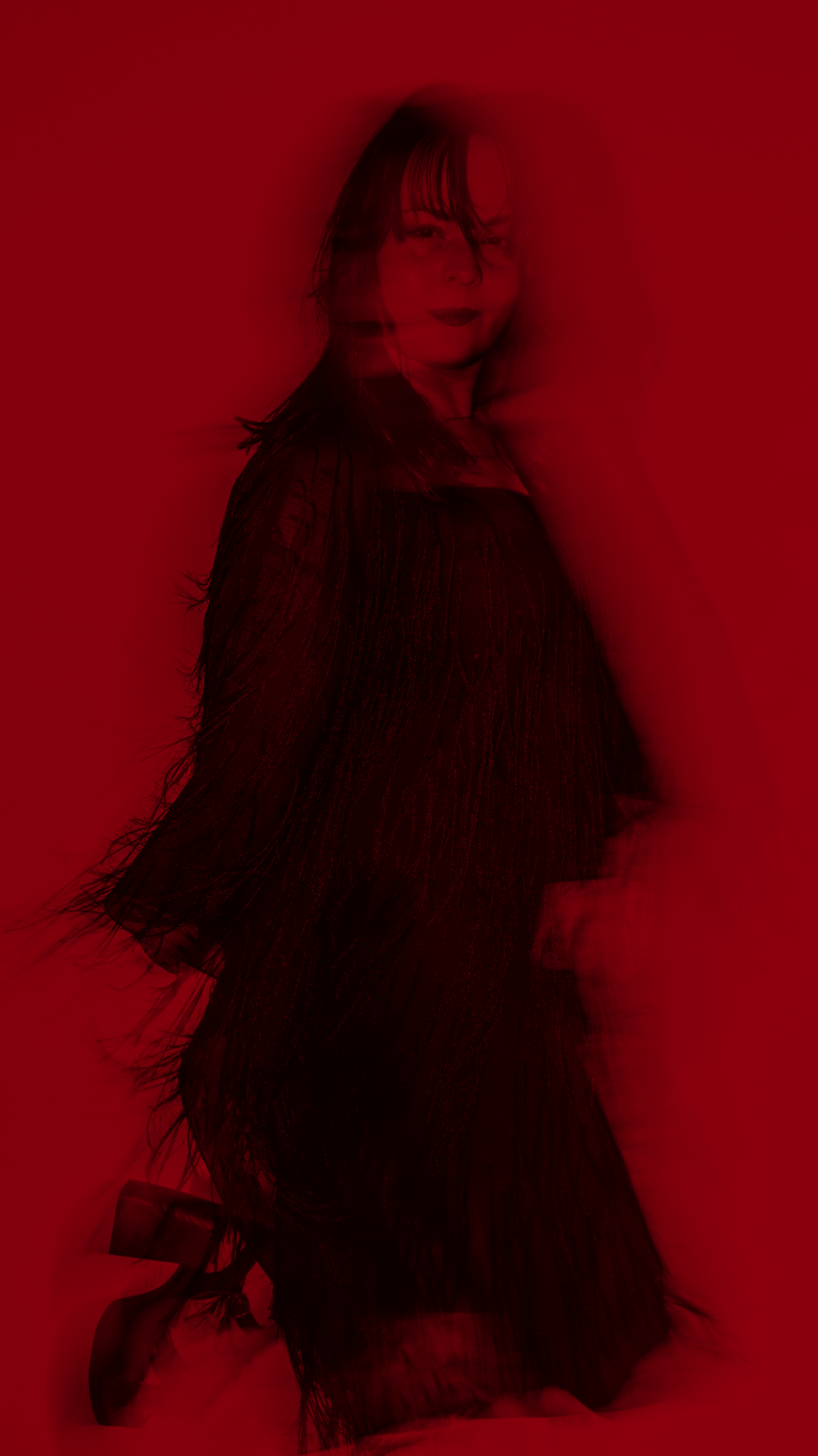Woman in black dress with fringes, standing against a red background.