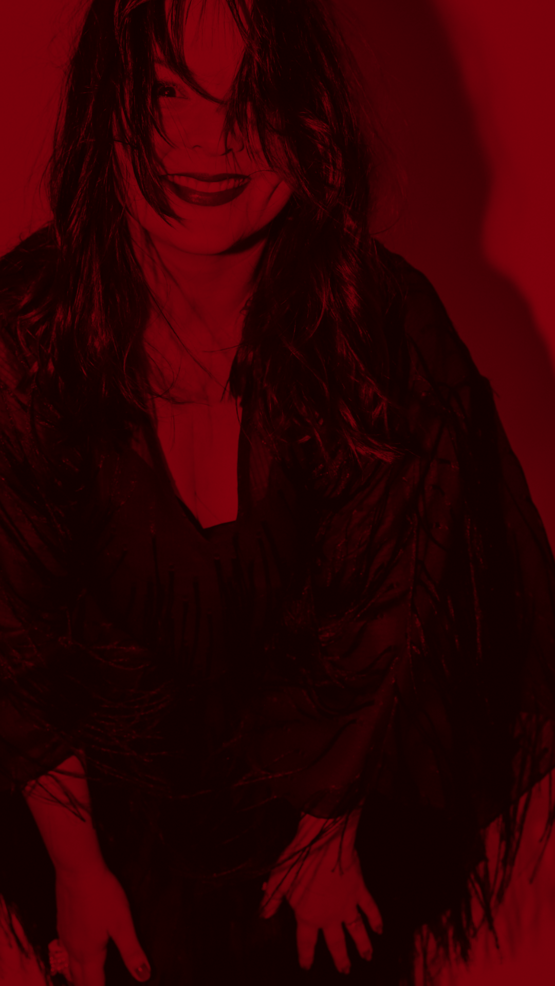A woman with wet hair smiles in a red-tinted photo, wearing a black sheer outfit.