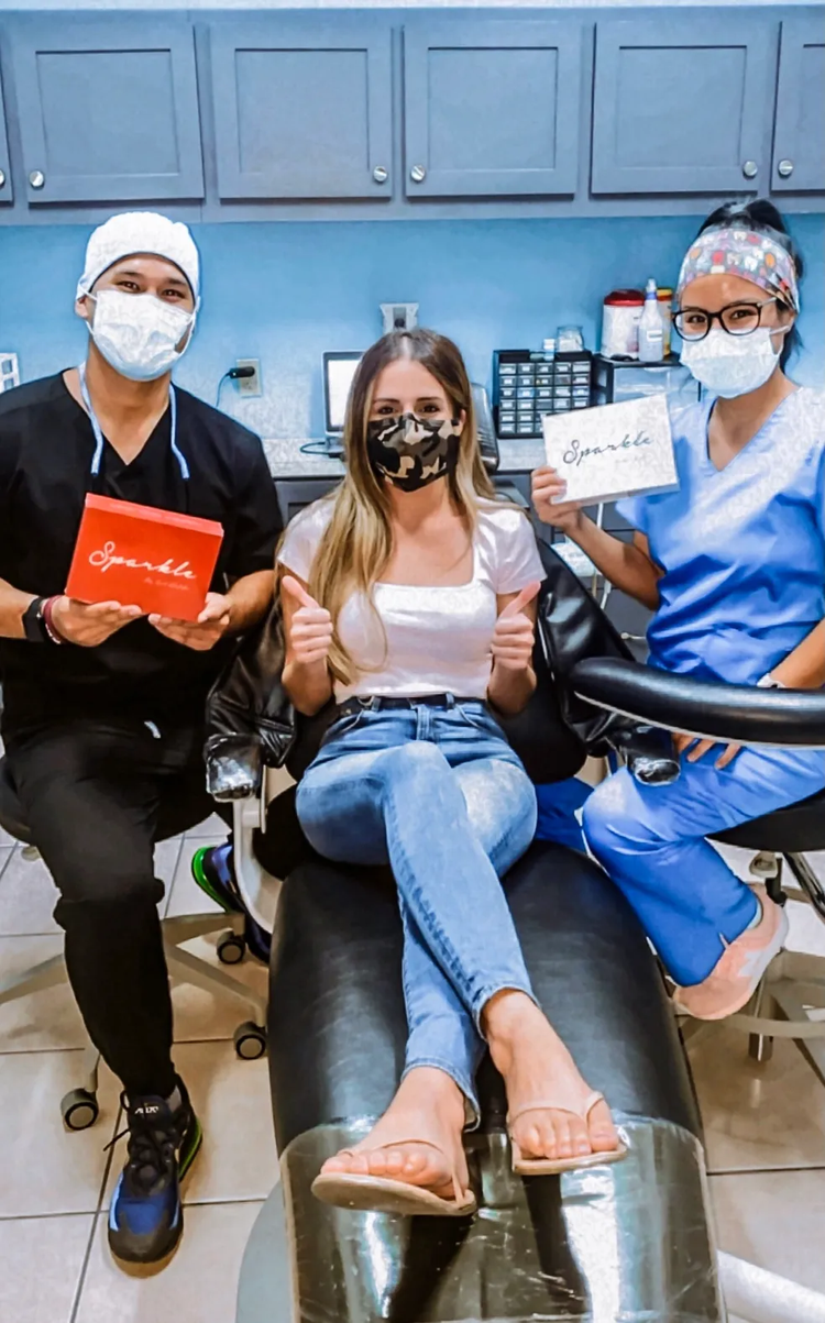 A customer holding a Sparkle Me White box with two dental office staff
