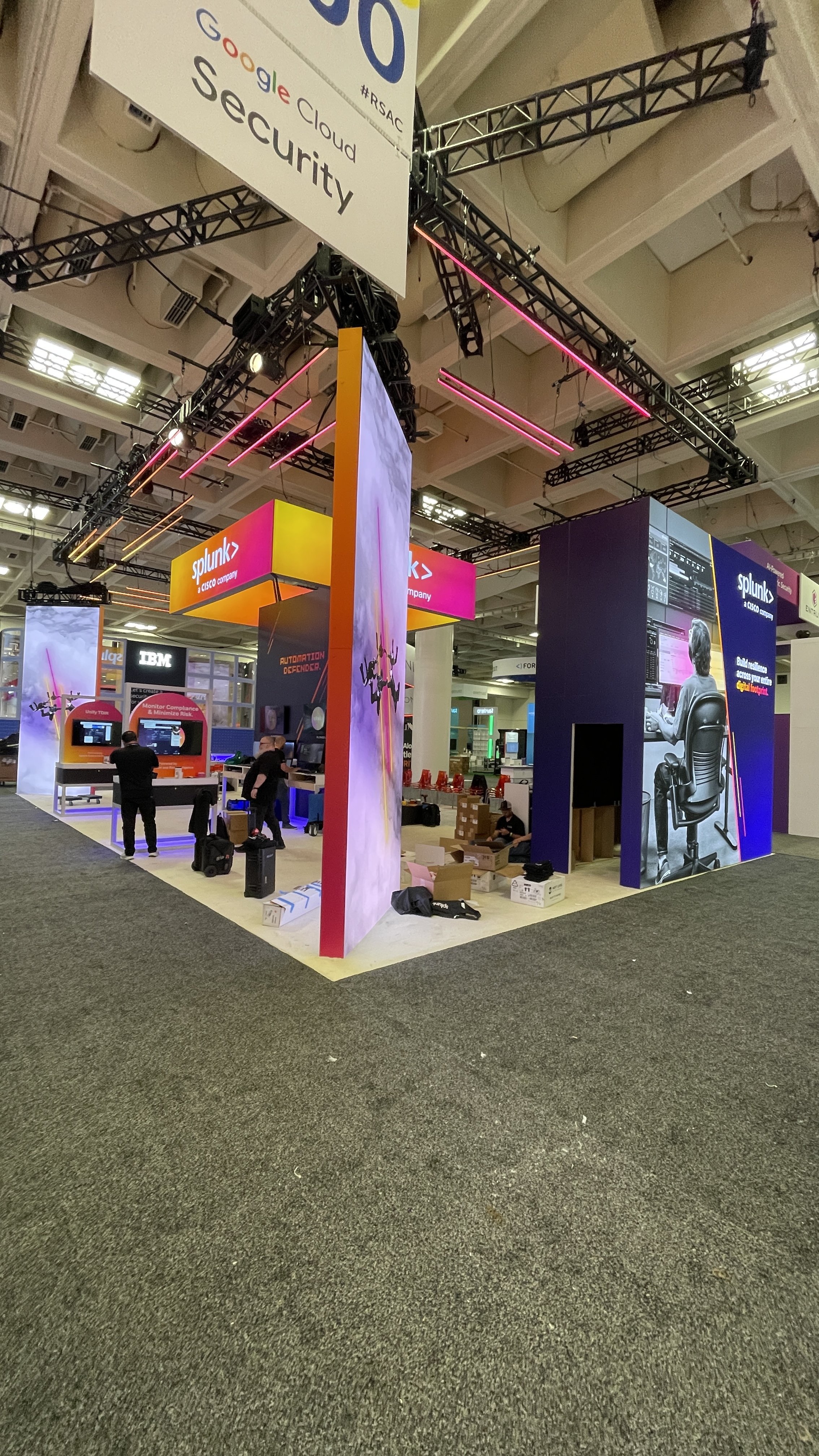 Showbox Exhibits Google Cloud Security and Splunk exhibition booth with neon lights and display monitors at a technology conference.