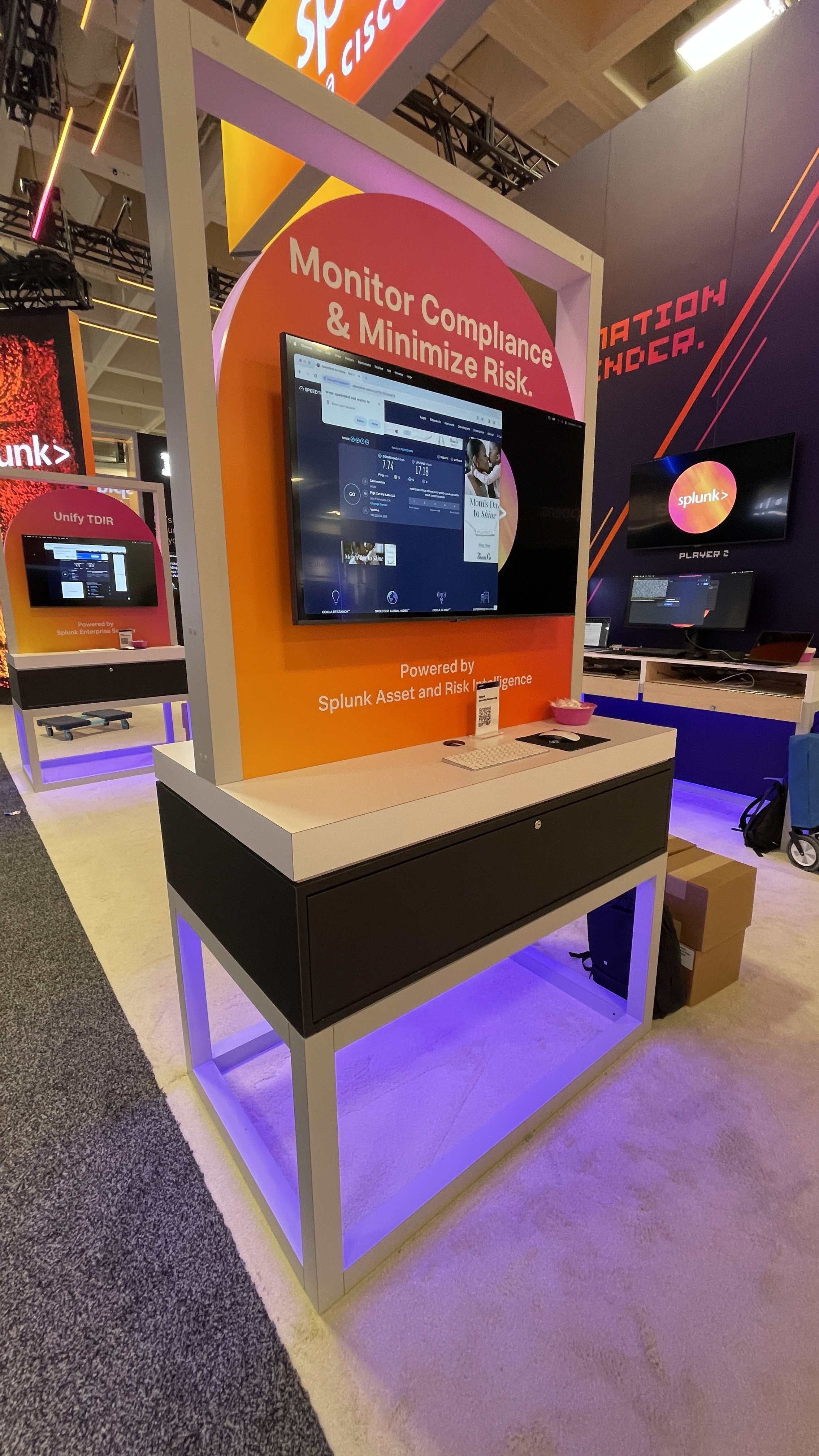 Showbox Exhibits Exhibition booth featuring Splunk display with "Monitor Compliance & Minimize Risk" message. A computer screen showcasing software, with text "Powered by Splunk Asset and Risk Intelligence."