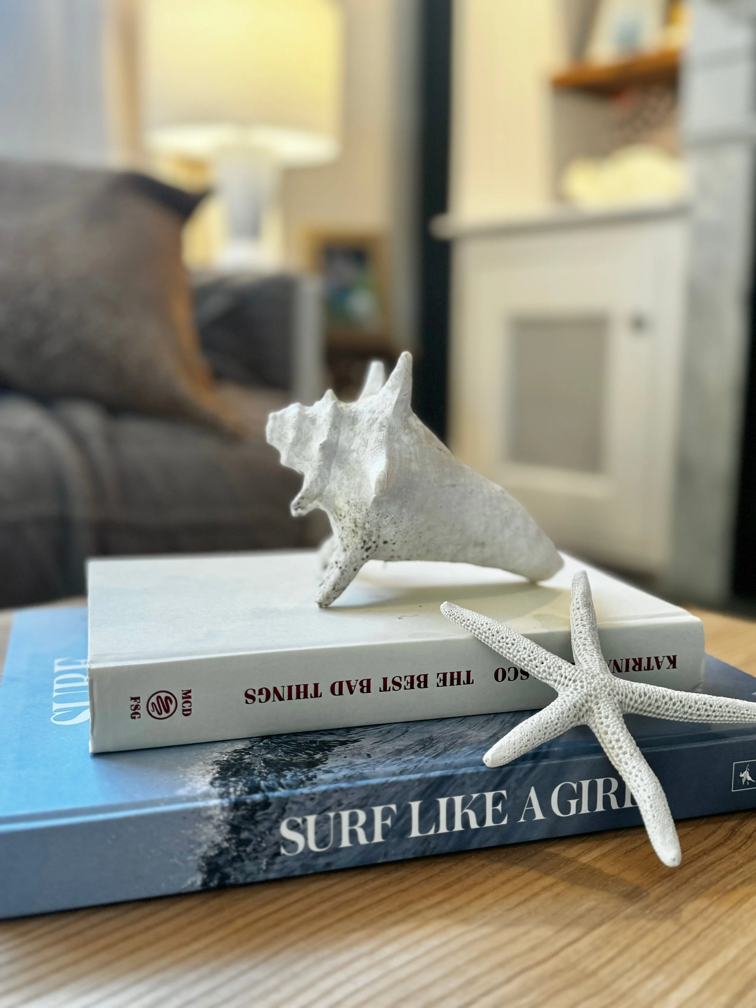 Two seashells, a starfish, and two books on a wooden table in a living room.