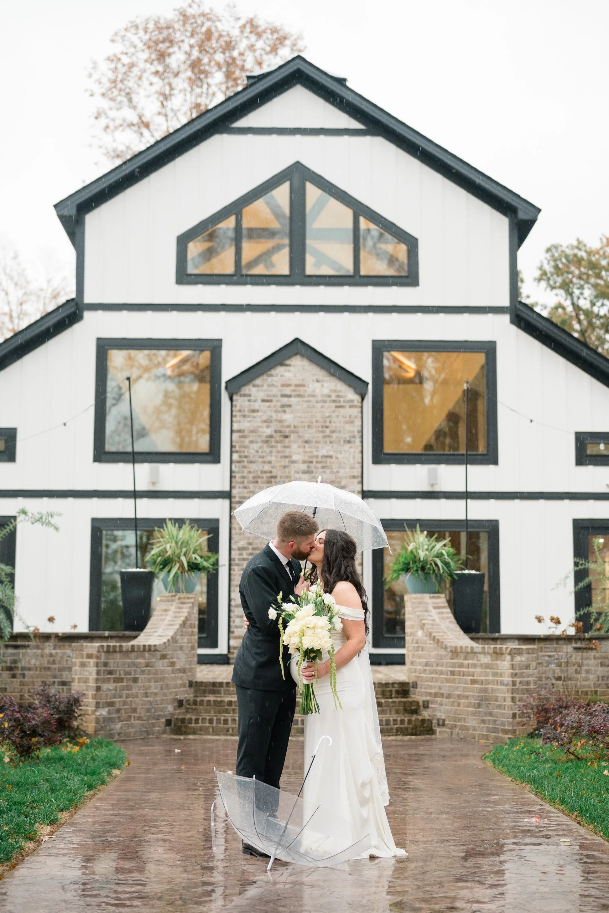 Bride and Groom Kissing in the outdoor area of black and white wedding venue in the rain milk and honey farms chapmansboro, TN