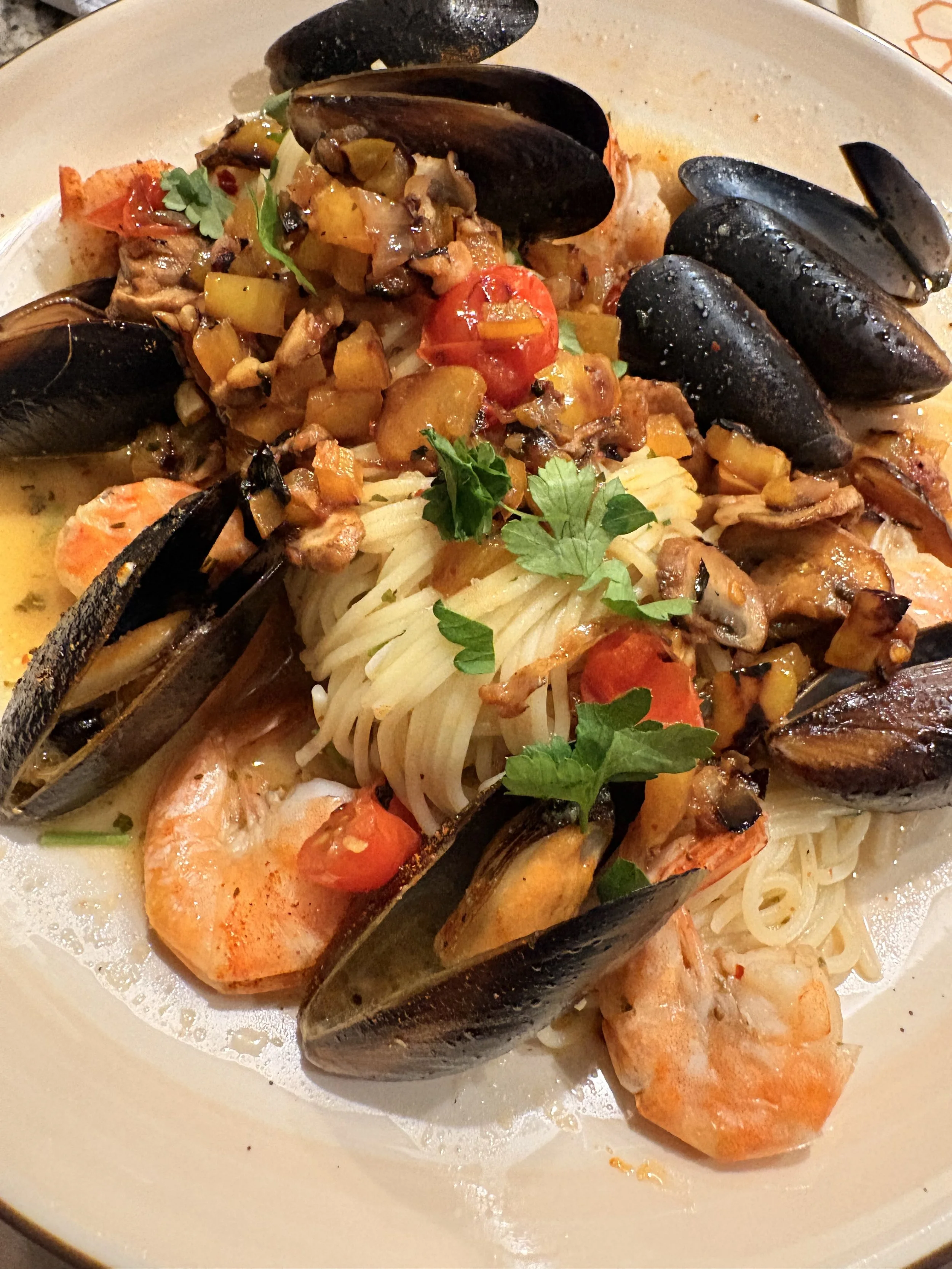 Seafood pasta dish with shrimp, mussels, cherry tomatoes, and chopped herbs.
