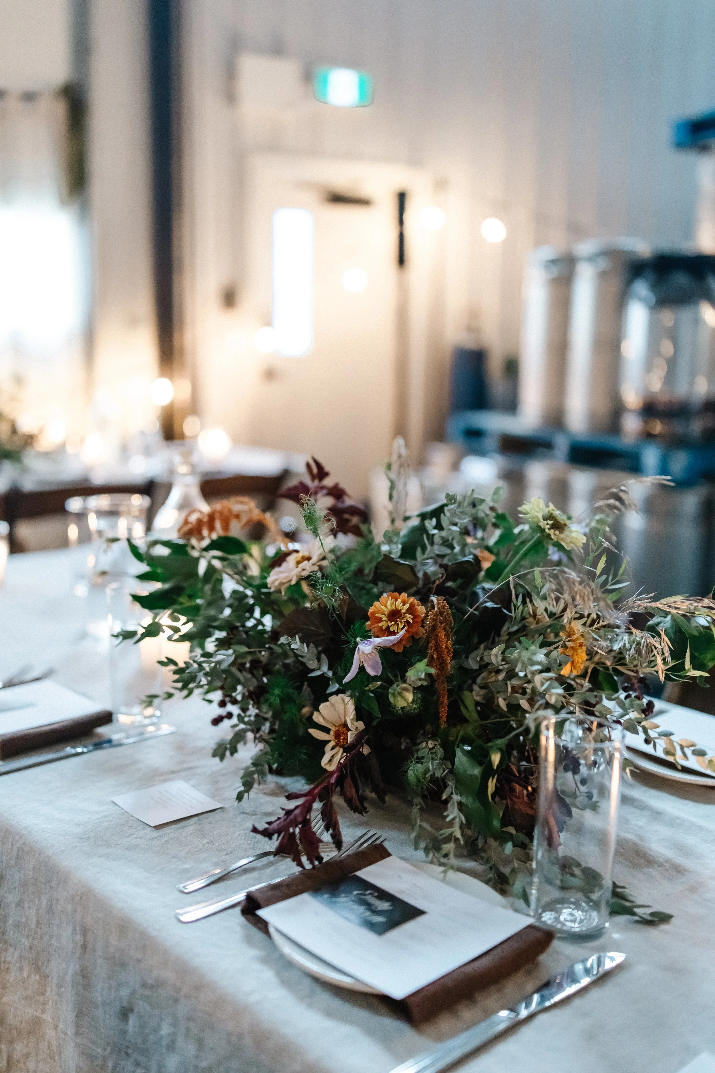 Elegant dinner table setup with a floral centerpiece, glassware, utensils, and napkins in a well-lit event space.