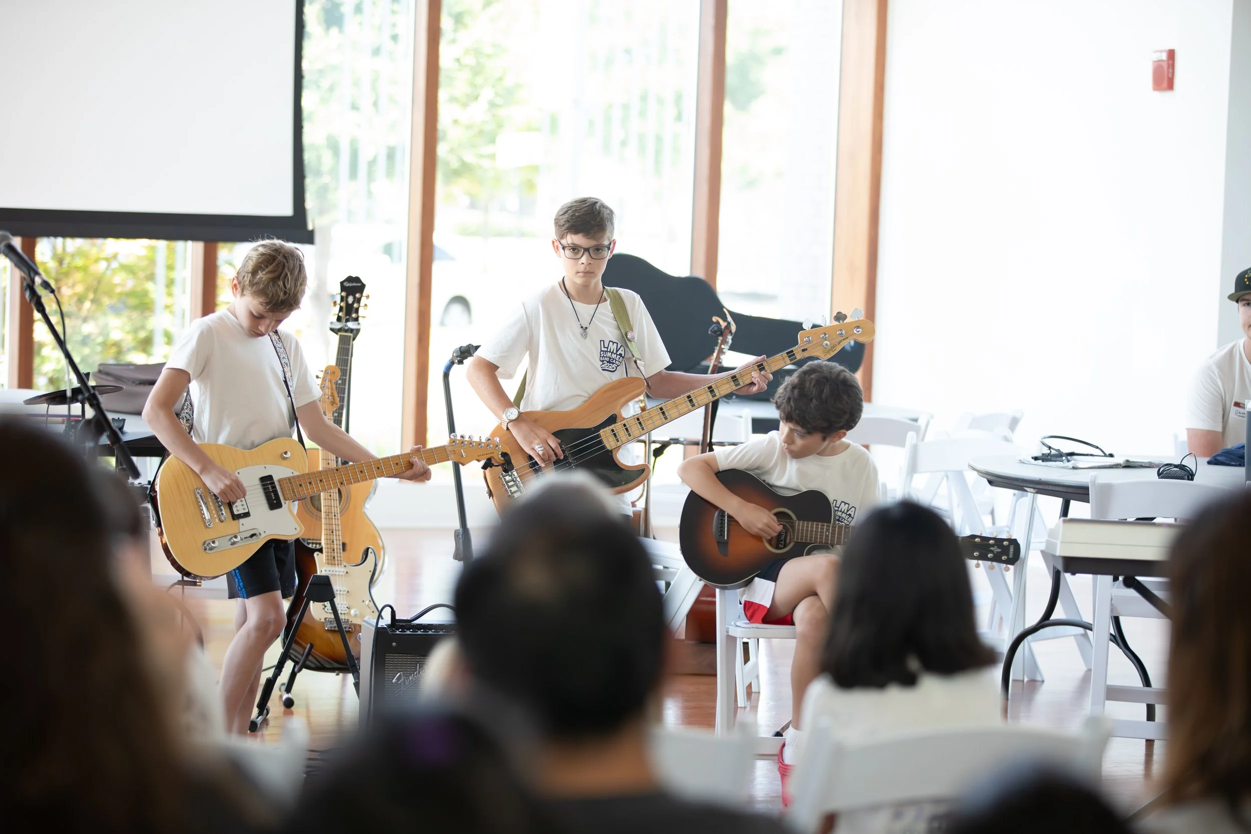 Young boys playing guitars during a music performance in a bright room with large windows at Summer Camp in Coppell Texas.