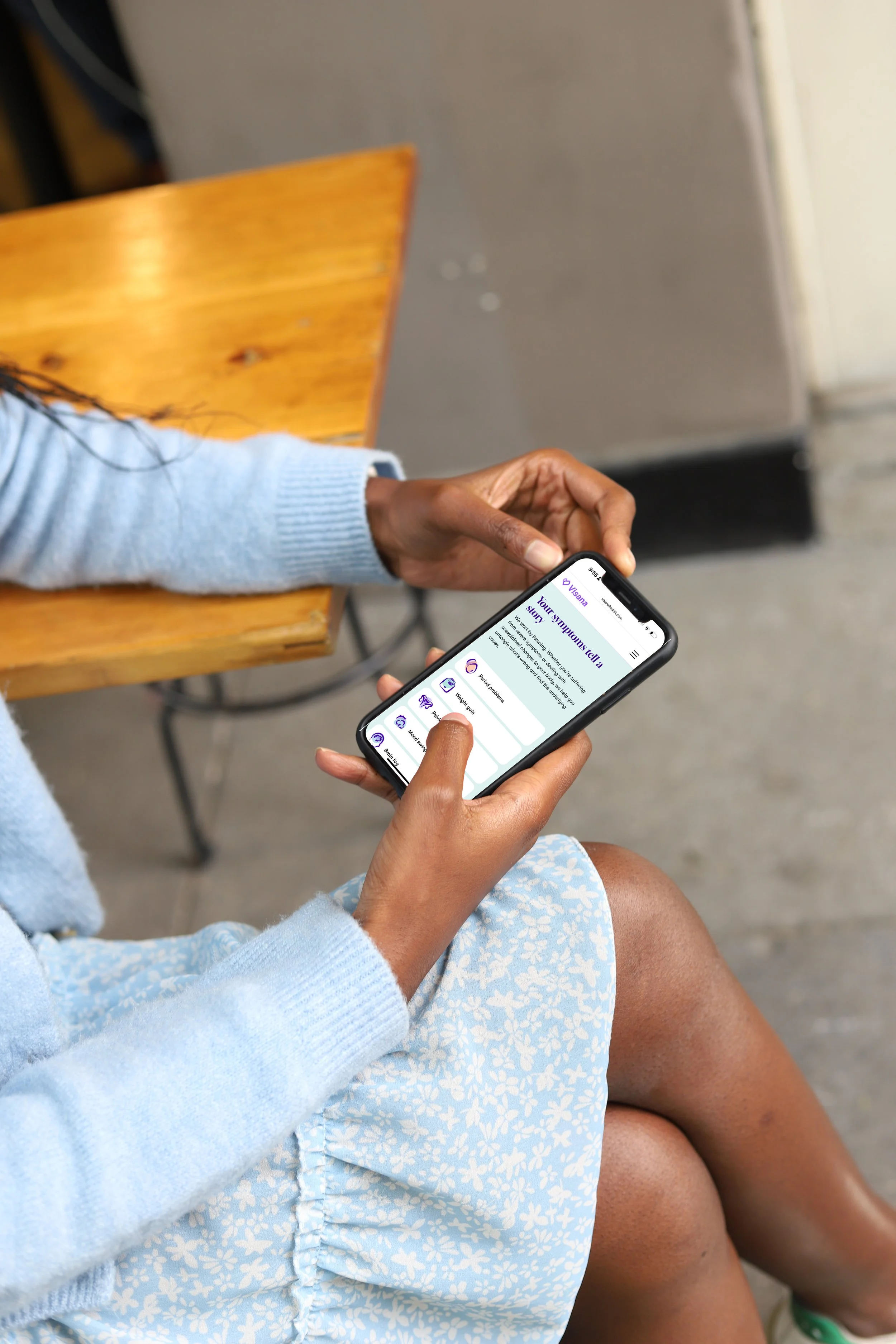 Person sitting on a wooden chair holding a smartphone with a health app open on the screen.