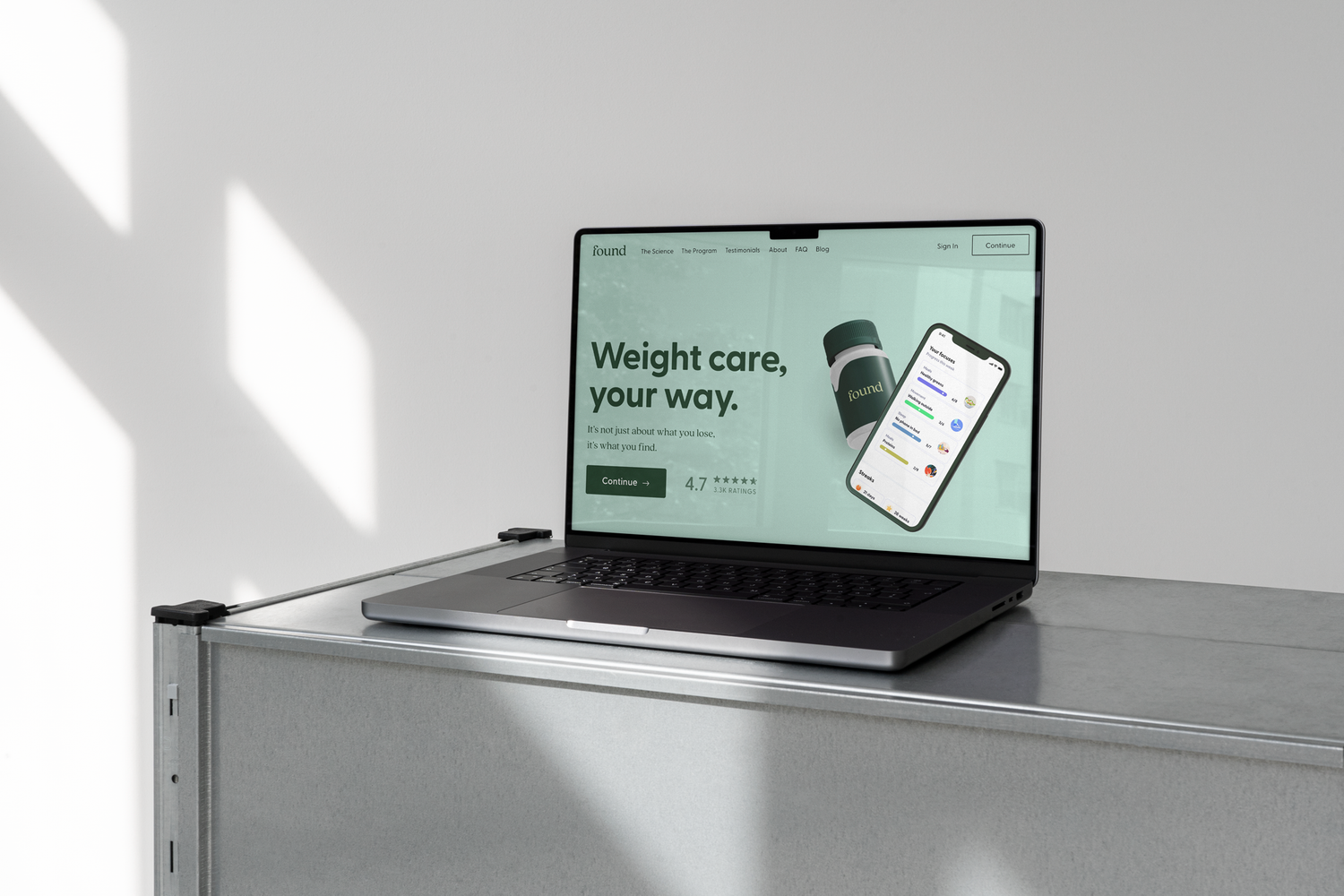 Laptop on a gray table displaying the website 'Found' with the slogan 'Weight care, your way,' and an app interface on a smartphone.