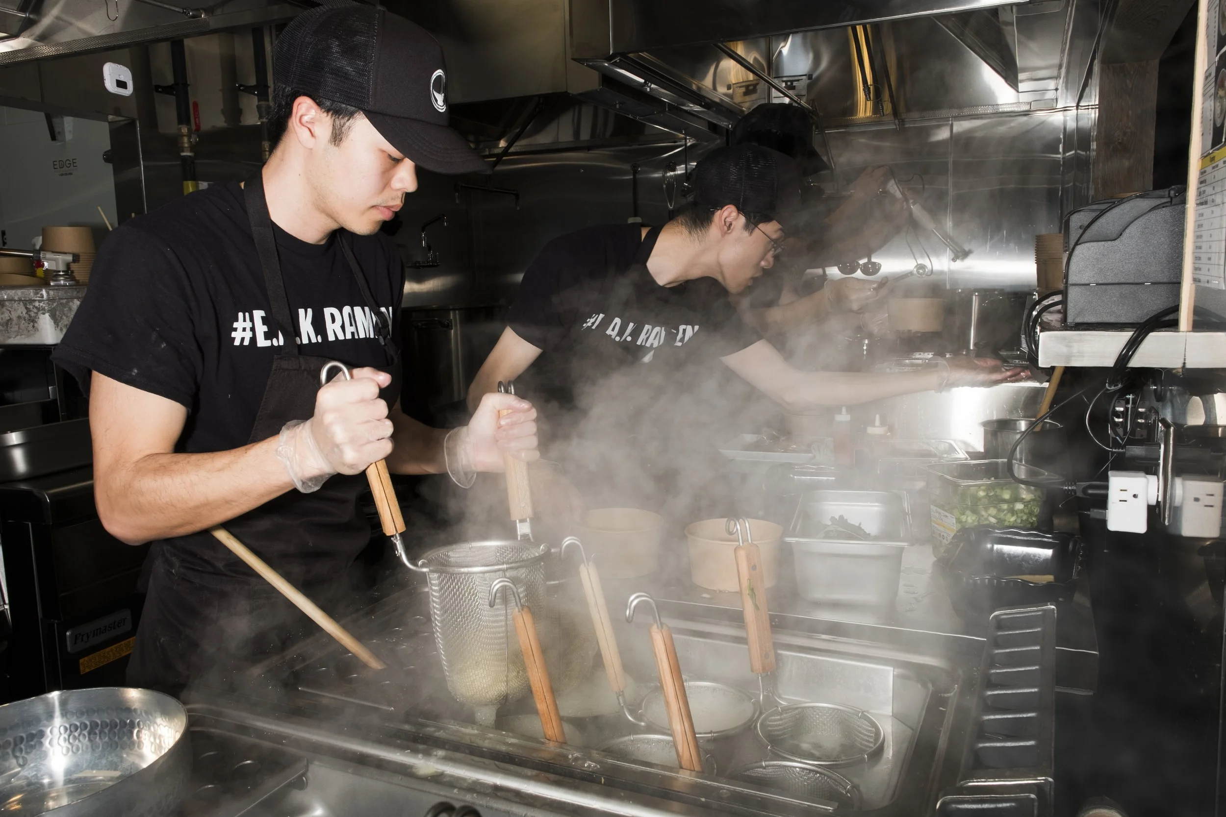 2 men cooking noodles in the back of house