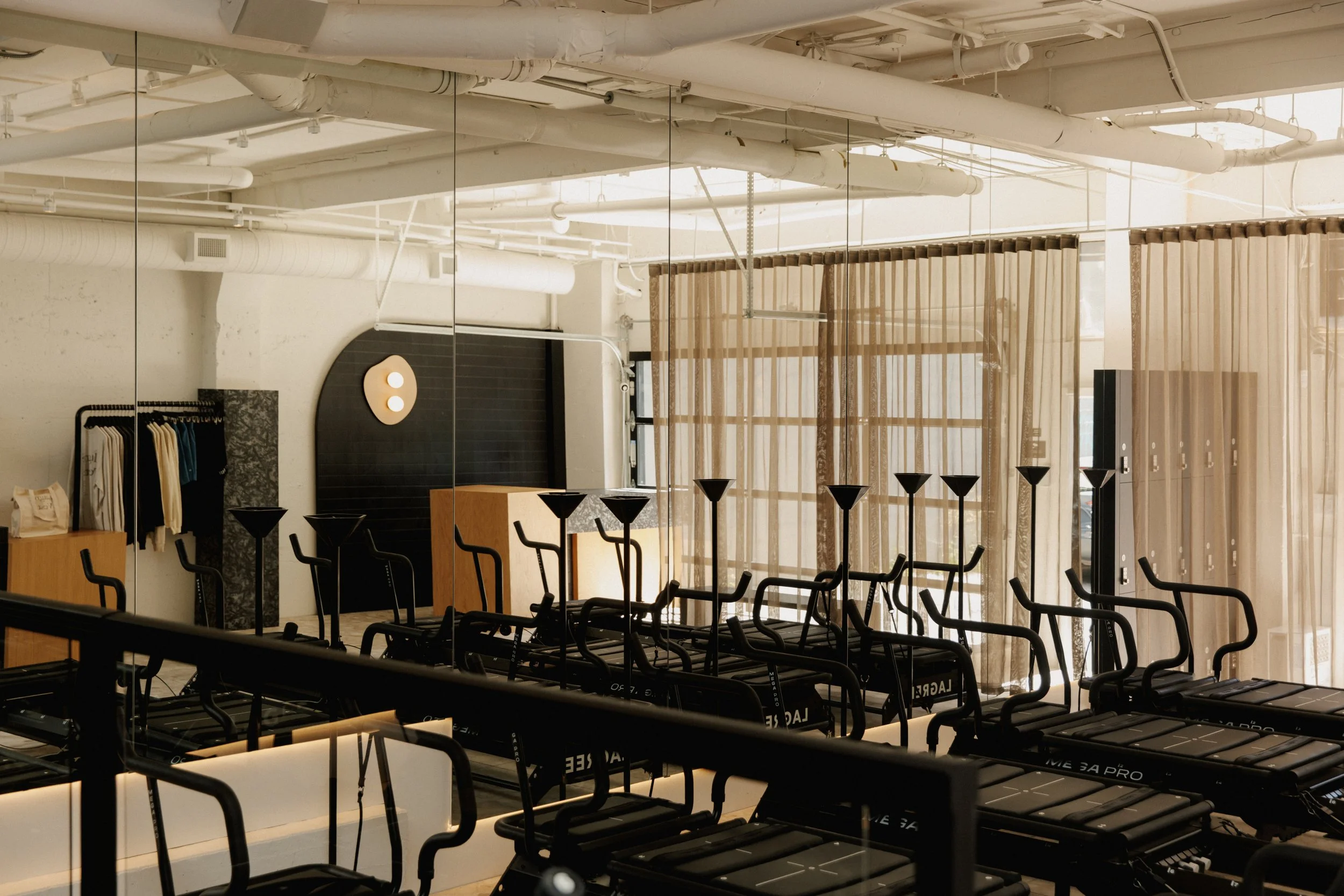 Mirrored wall in reformer pilates studio with merchandising and sheer beige curtains dividing the space.