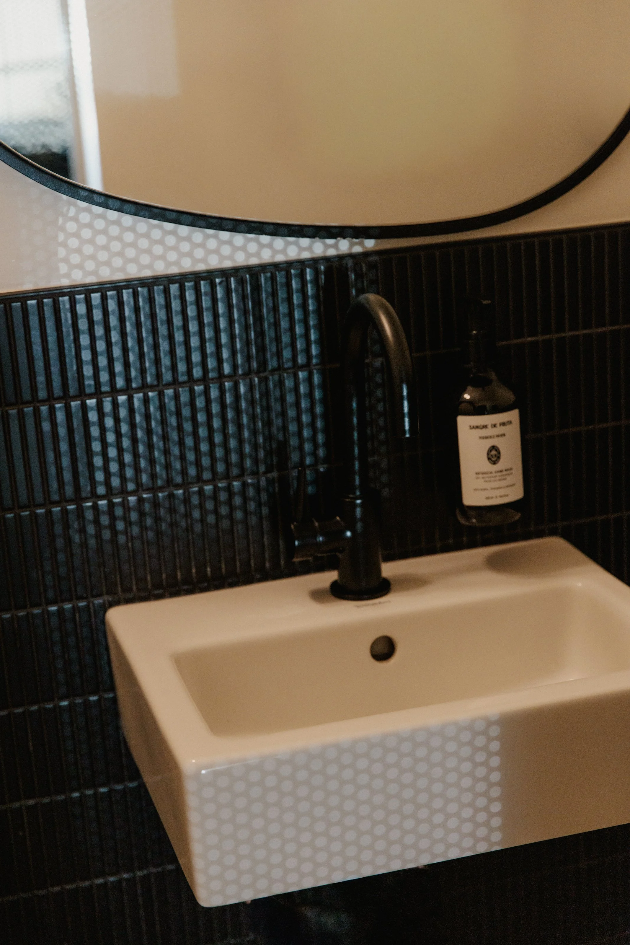 Black tiled bathroom with white minimally designed sink.