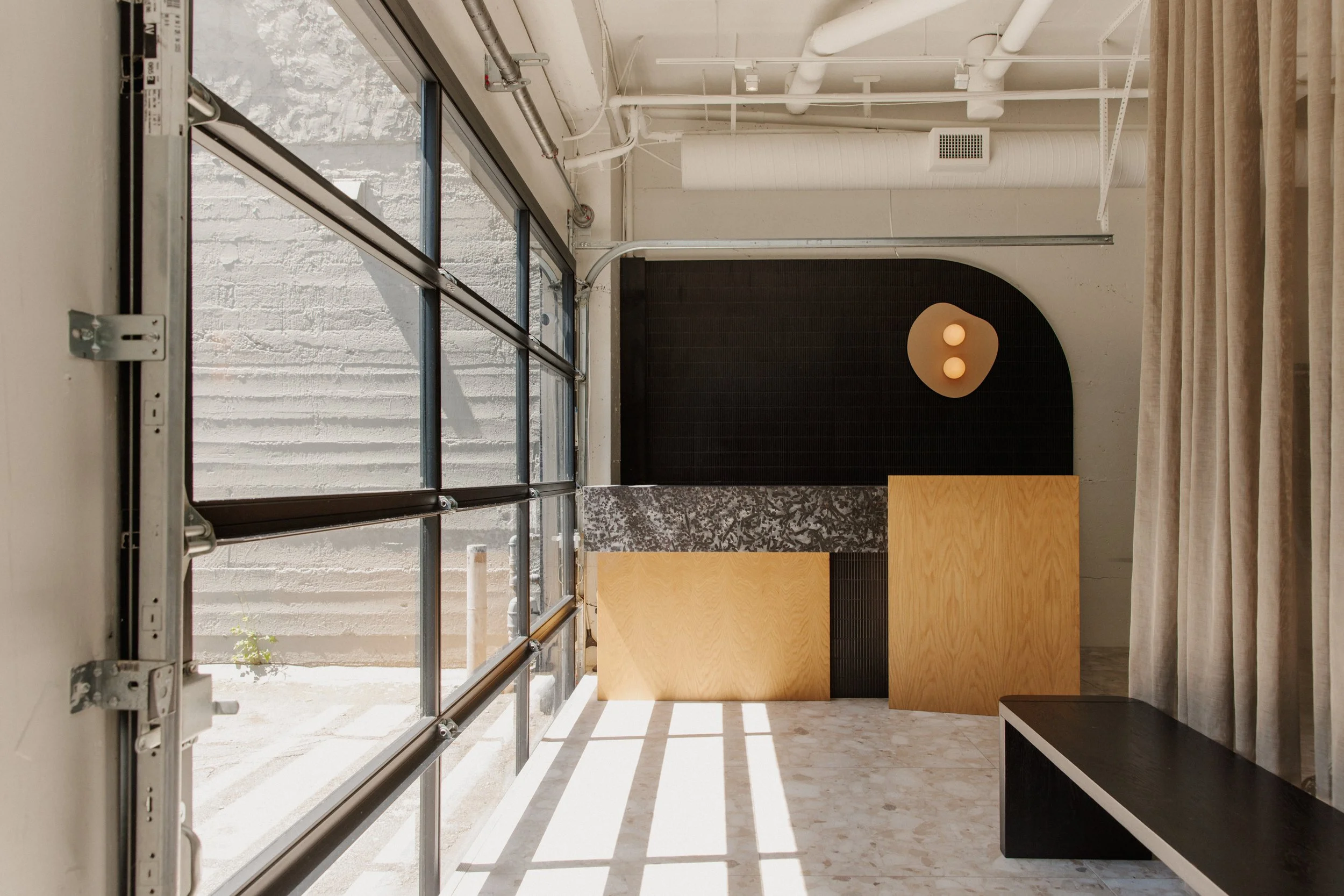Entrance of pilates studio with simple wood and stone reception desk, curved black wall and minimal 2 bulb light fixture.