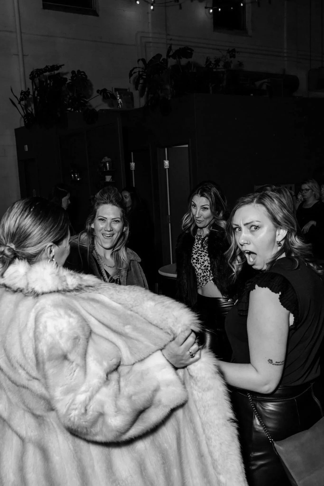 A group of women gathered closely together, with one woman arm-wrestling another. The women appear to be in a cheerful, lively environment, possibly at a party or social event.