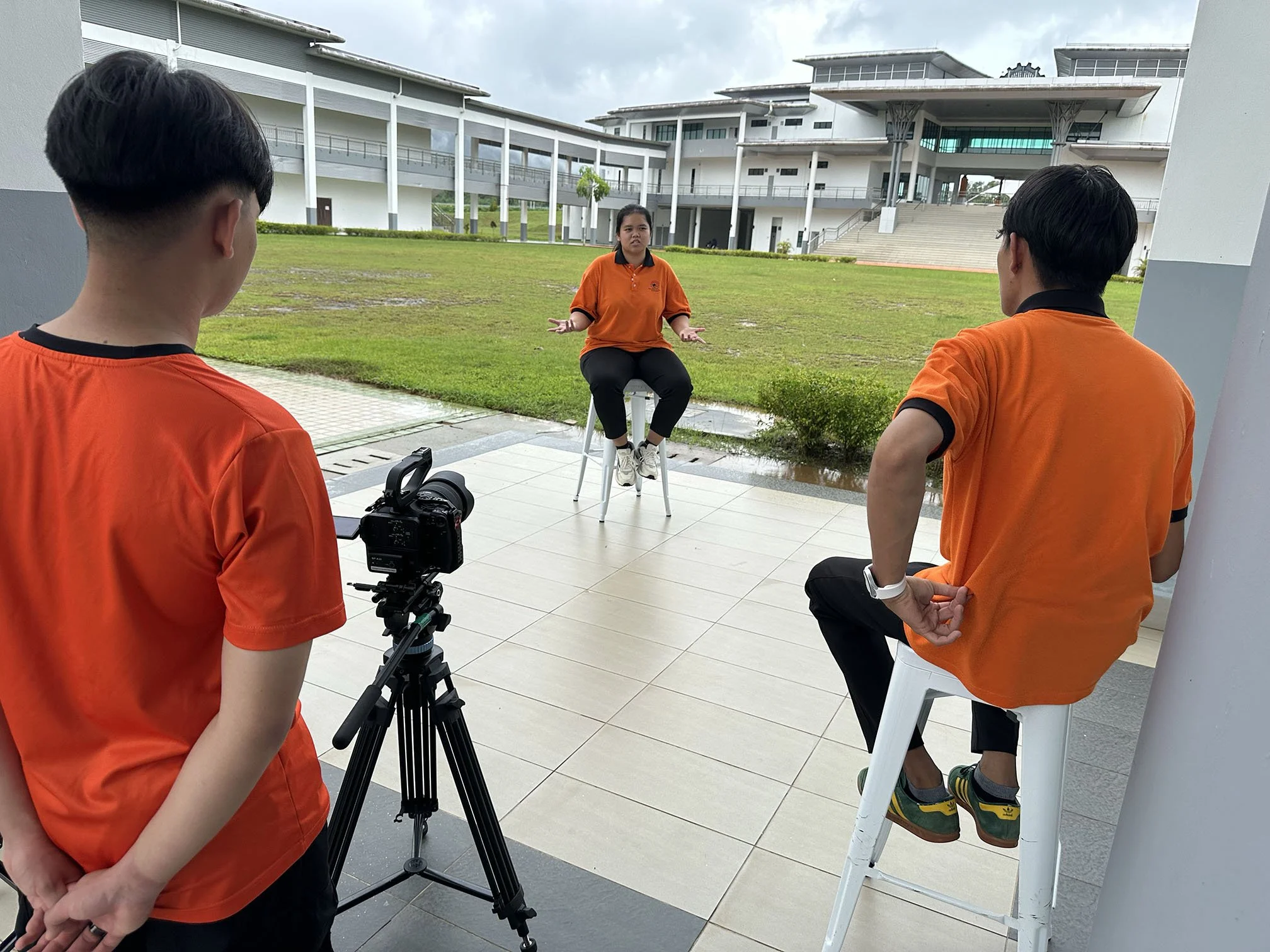Instructor guiding CENTEXS Lundu students through an on-location corporate interview filming session using professional production equipment