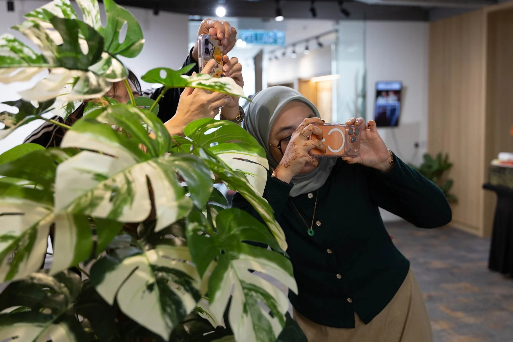 Participant using her smartphone to practise creative composition by photographing through leaves during a photography exercise.