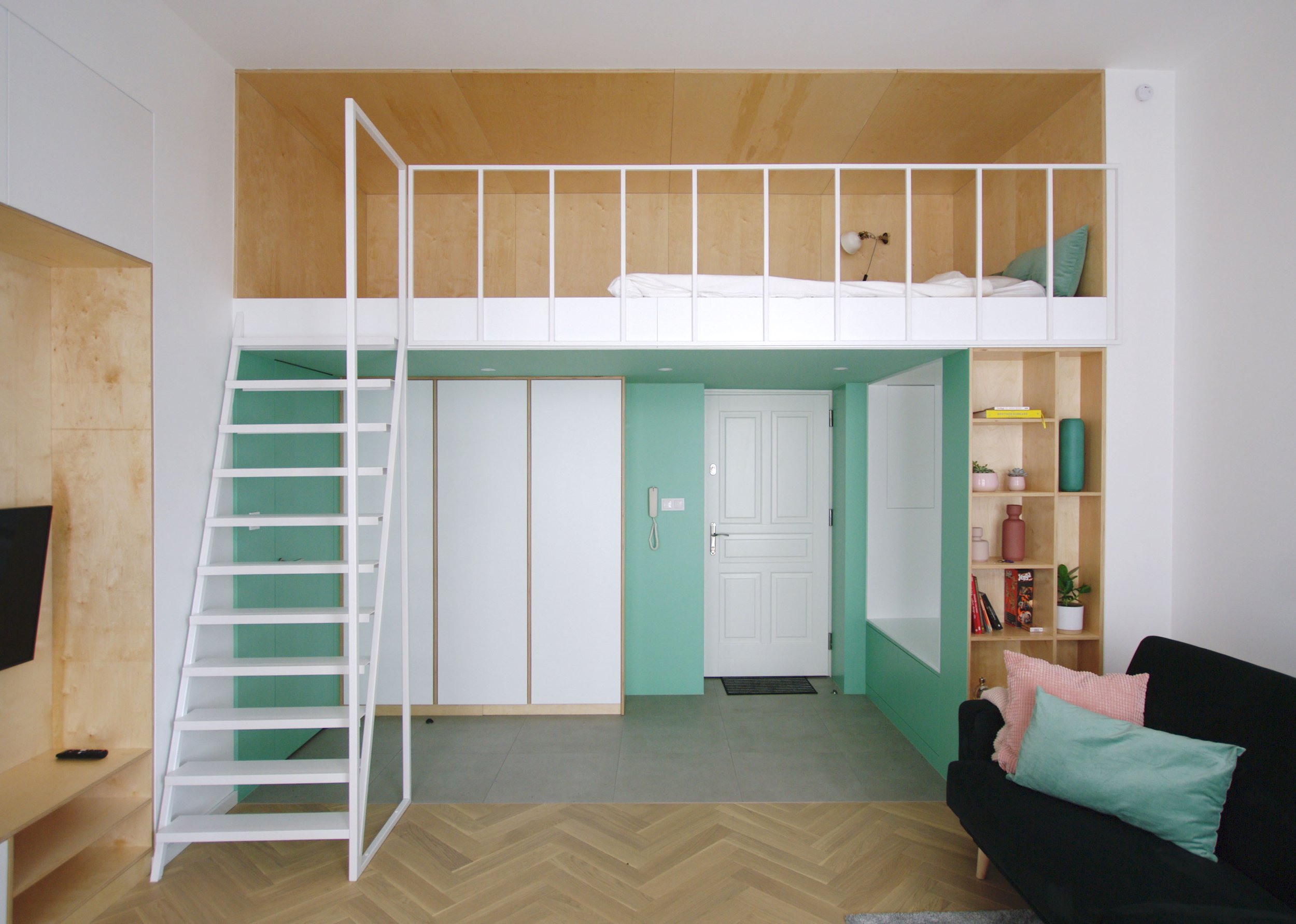Front view of the mezzanine bedroom at Apartment 30, with white stairs and railings above fitted storage and the entrance hall.