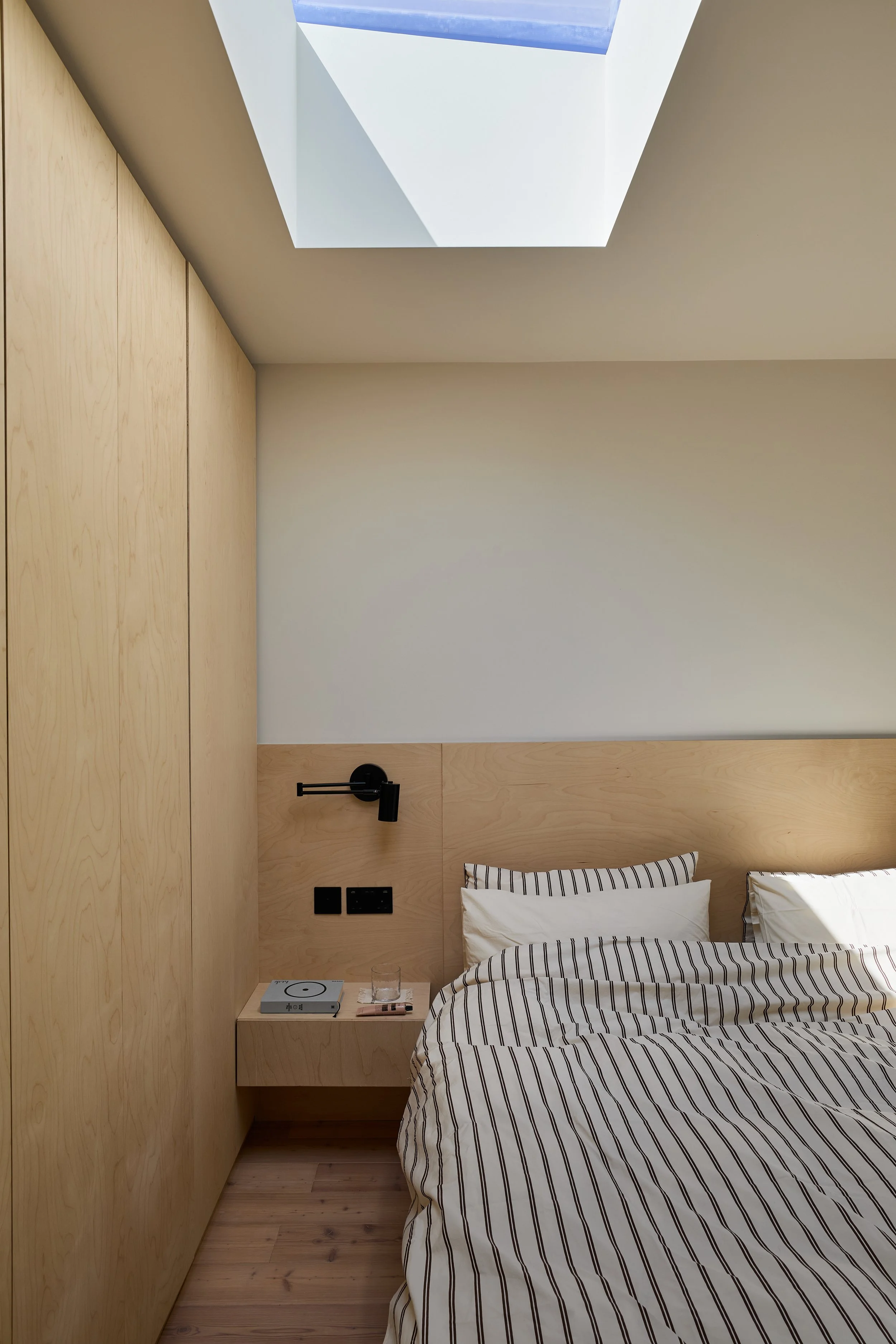 Loft bedroom at Norwood House, showing a rooflight above the bed, a black reading light and built-in timber storage.
