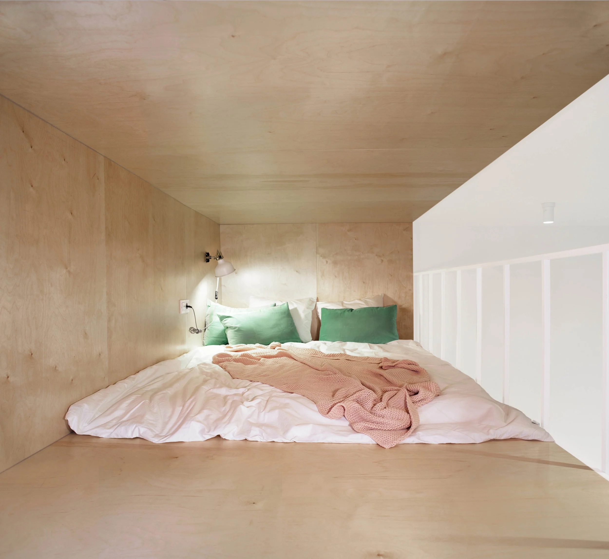 Timber-lined mezzanine bedroom at Apartment 30, with green cushions, pink bedding and a white balustrade.