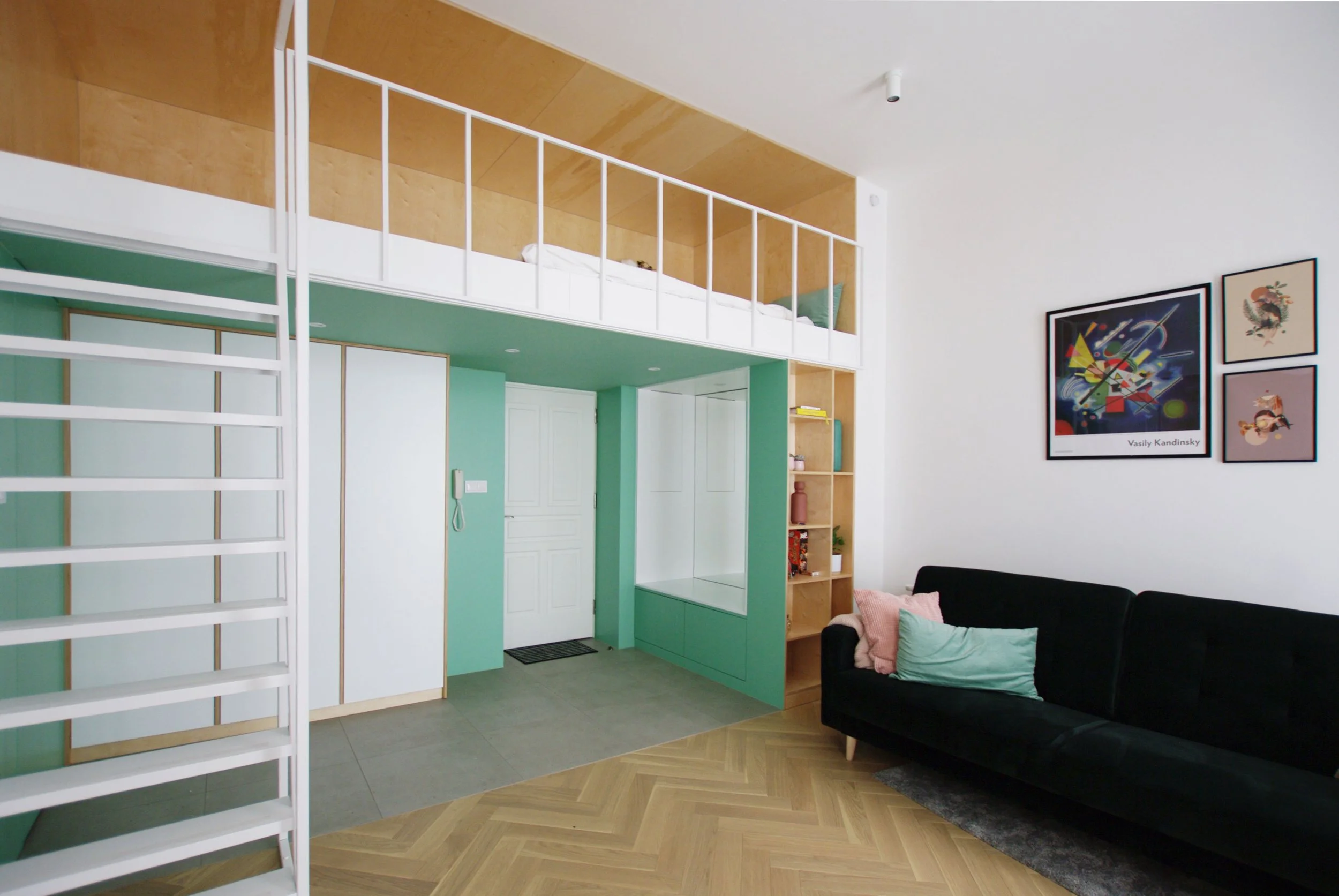 Living area at Apartment 30, with a black sofa, framed artwork, mint-green walls and a timber-lined mezzanine above fitted storage.
