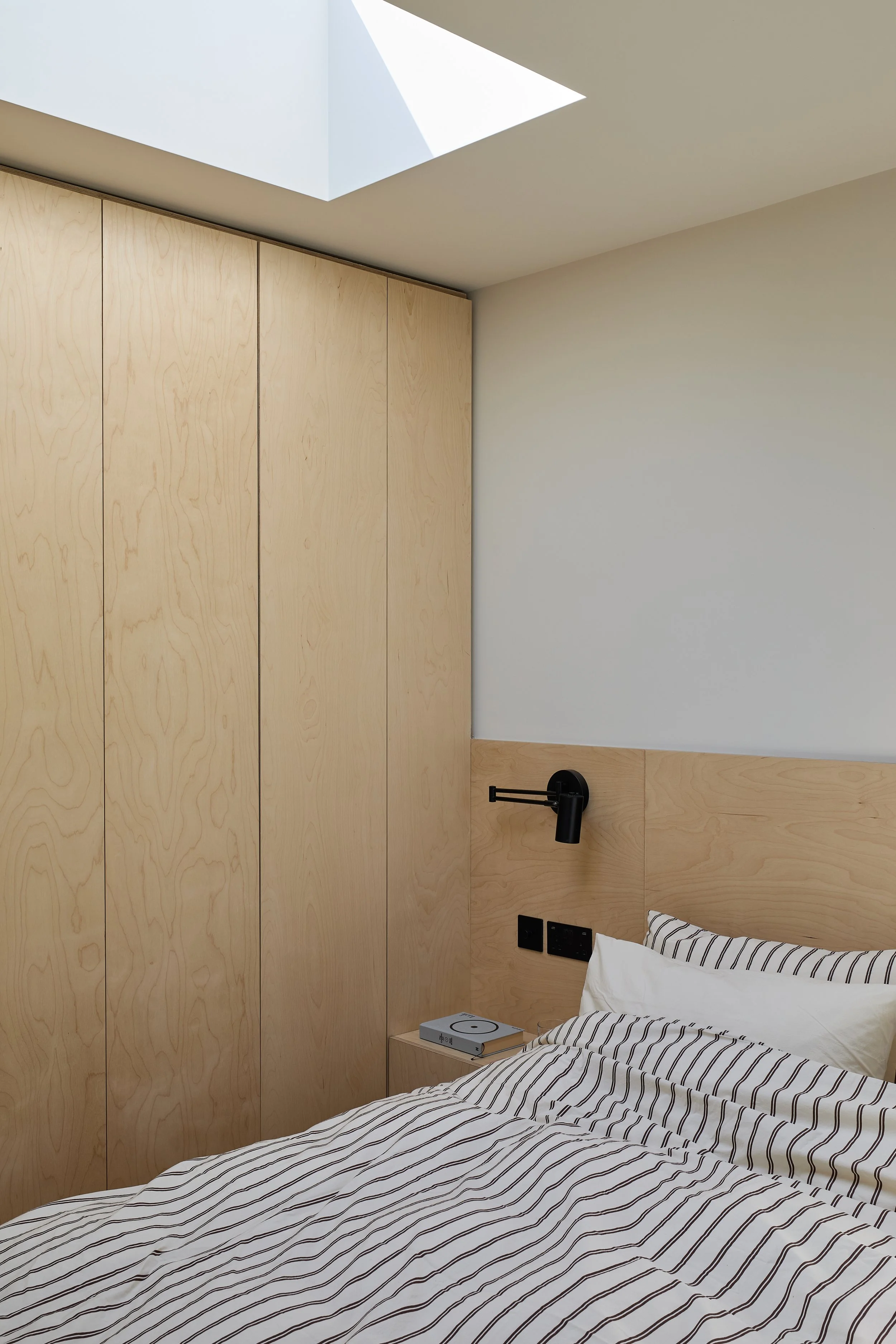 Loft bedroom at Norwood House, with full-height timber wardrobes, a matching headboard, striped bedding and a rooflight.
