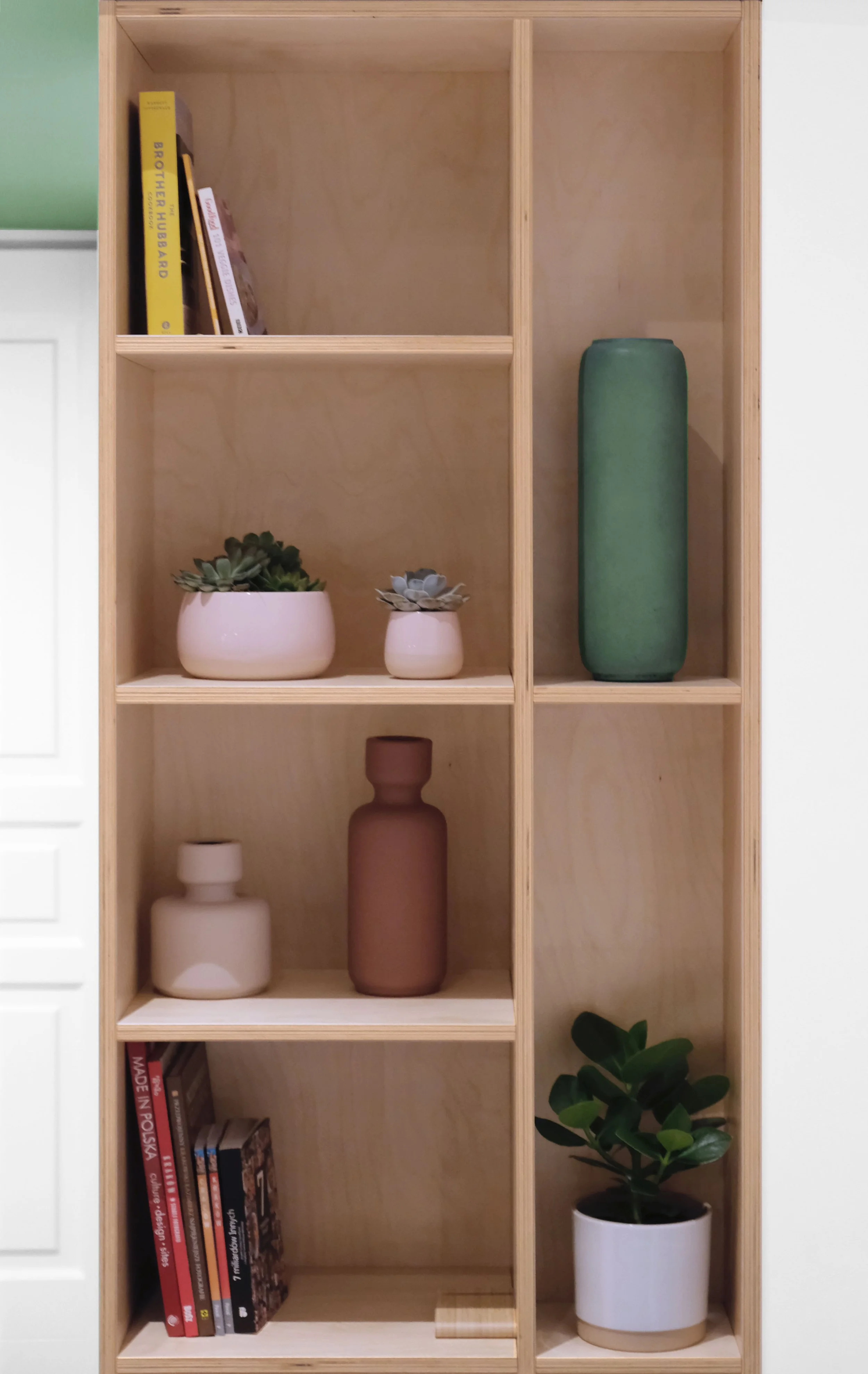 Timber display shelving at Apartment 30, with potted plants and ceramic vases in green, pink and terracotta tones.