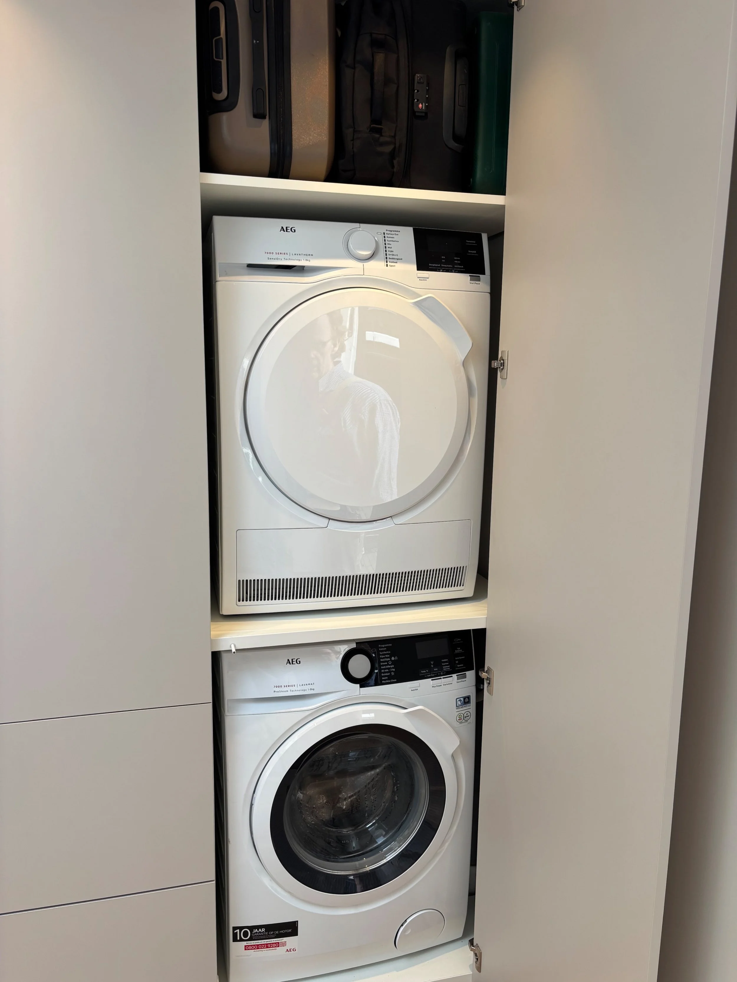 Geopende wasmachinekast in Laren met gestapelde wasmachine en droger en opbergruimte