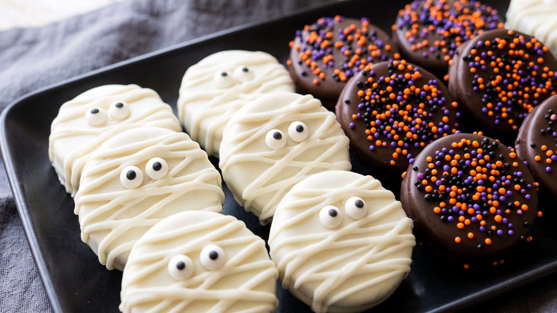 Oreo cookies dipped in candy melts and decorated with sprinkles in the center. The cookies on the left are dipped and decorated to look like Halloween mummies.