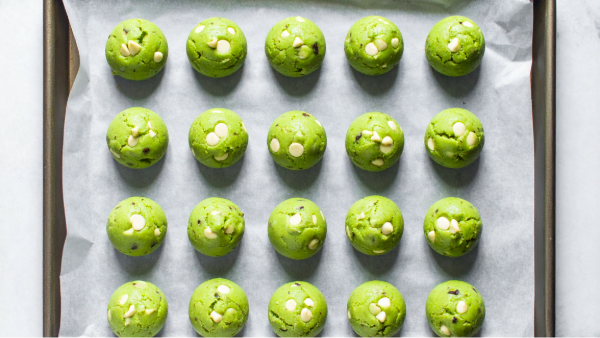 Green cake mix cookie dough with white chocolate chips scooped onto a parchment-lined baking sheet, ready to bake