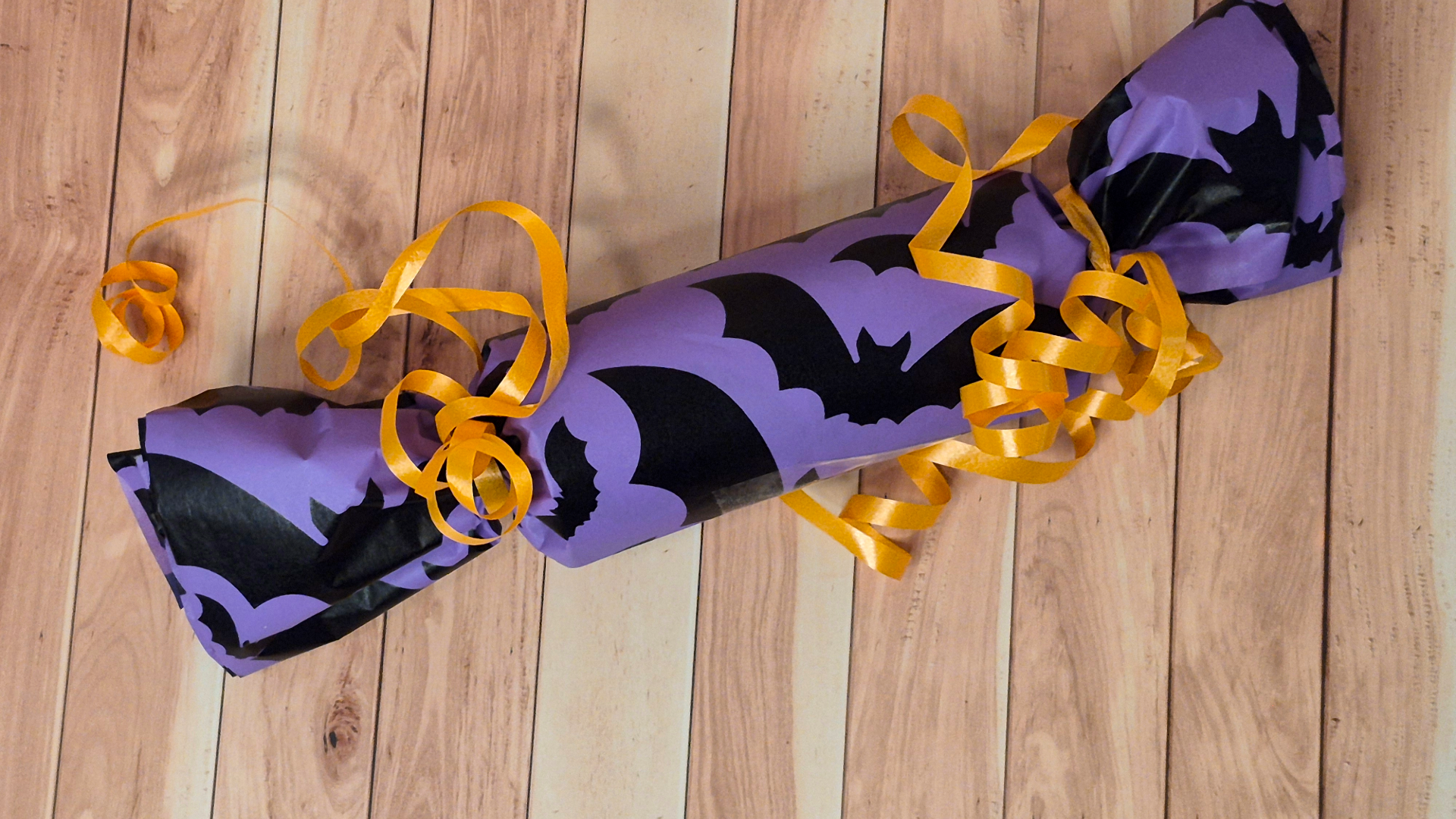 Completed Halloween favor cracker fully wrapped and decorated with orange curling ribbon.