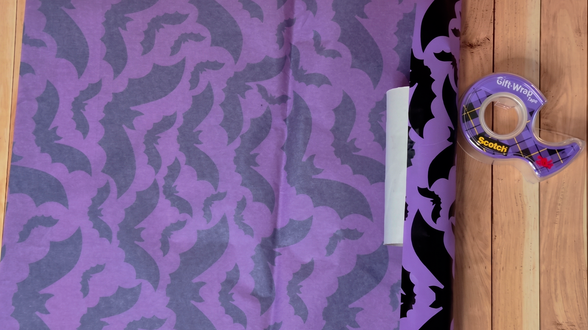 Halloween-themed tissue paper being wrapped around a paper tube for a Halloween favor cracker craft.