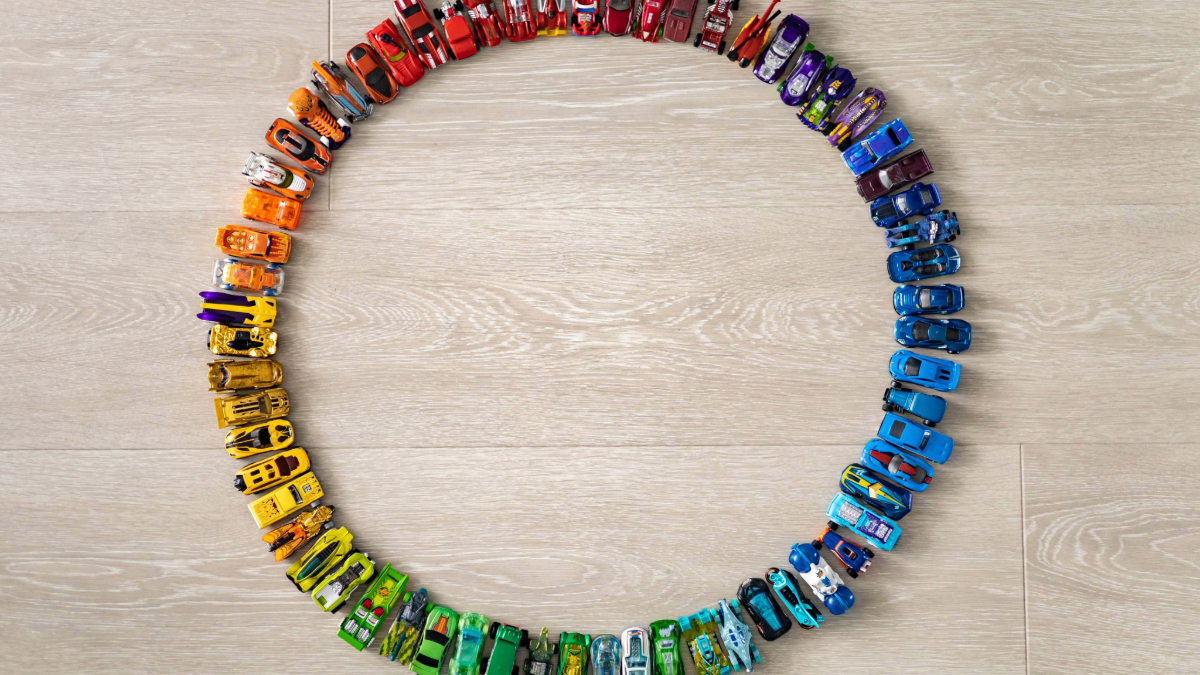 A creative circle of colorful Hot Wheels toy cars organized by color on a light wood floor, showcasing a simple and manageable toy car storage system for children.