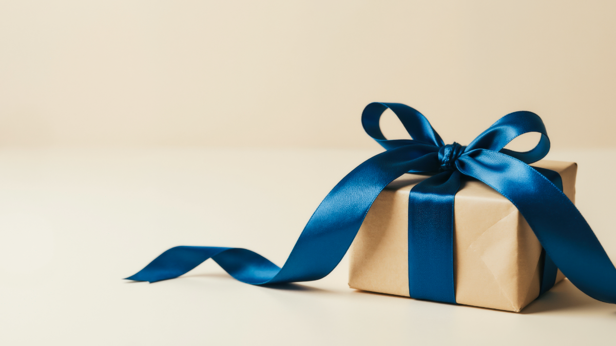 A single, beautifully wrapped brown kraft paper gift box with a large blue satin ribbon, set against a cream-colored background, illustrating polite kids' birthday party gift registry ideas.