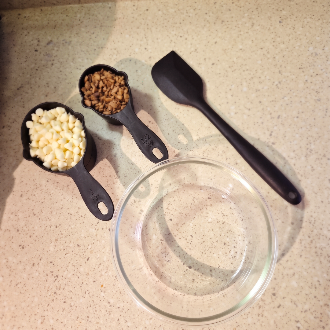 Vanilla baking chips and cocoa krispies in measuring cups next to a spatula and bowl, prepped for making reverse crunch bars.