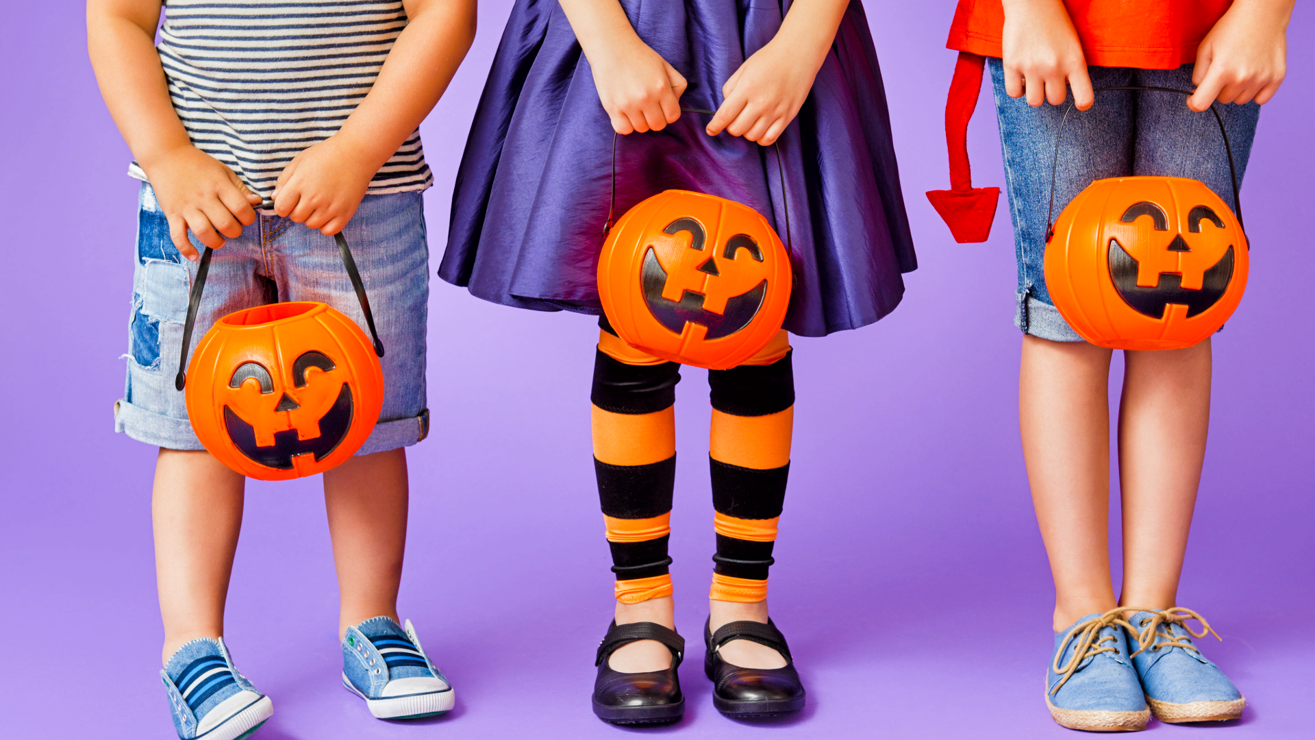 Three young children in halloween costumes and holding trick-or-treat pumpkins who don't have on enough layers for a cold Halloween night