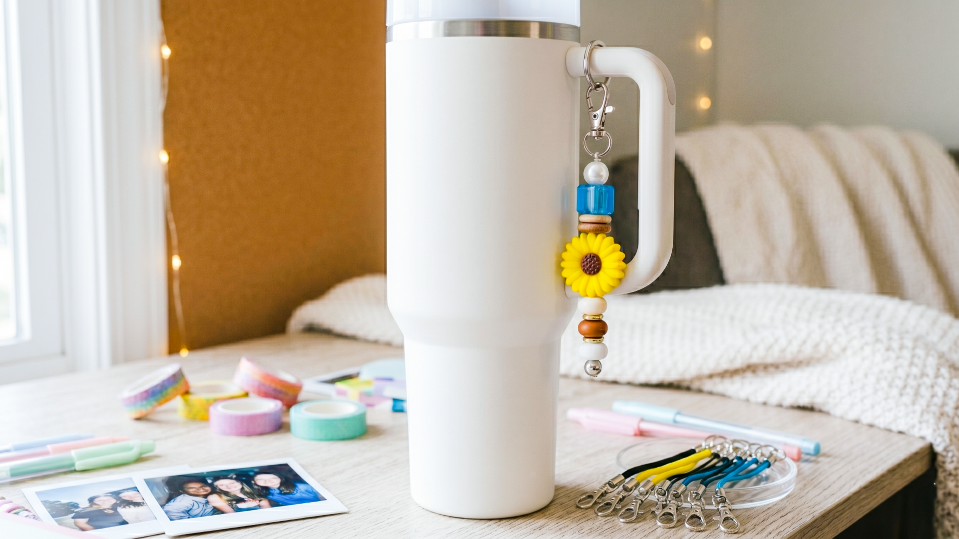 Tween desk set up with a Stanley-style tumbler and a tumbler keychain decorated with charms. The desk also has washi tape, pens, and leather cords laid out for a charm bar party.