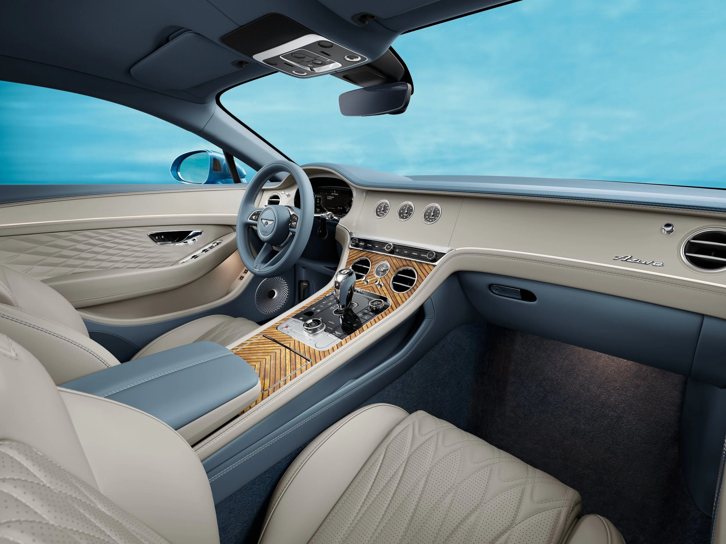 The interior of a luxury car with beige leather seats and a wooden center console. The dashboard features several gauges and controls, and the steering wheel has a logo in the center. The view includes a rearview mirror and part of the car's ceiling with built-in lights and controls.