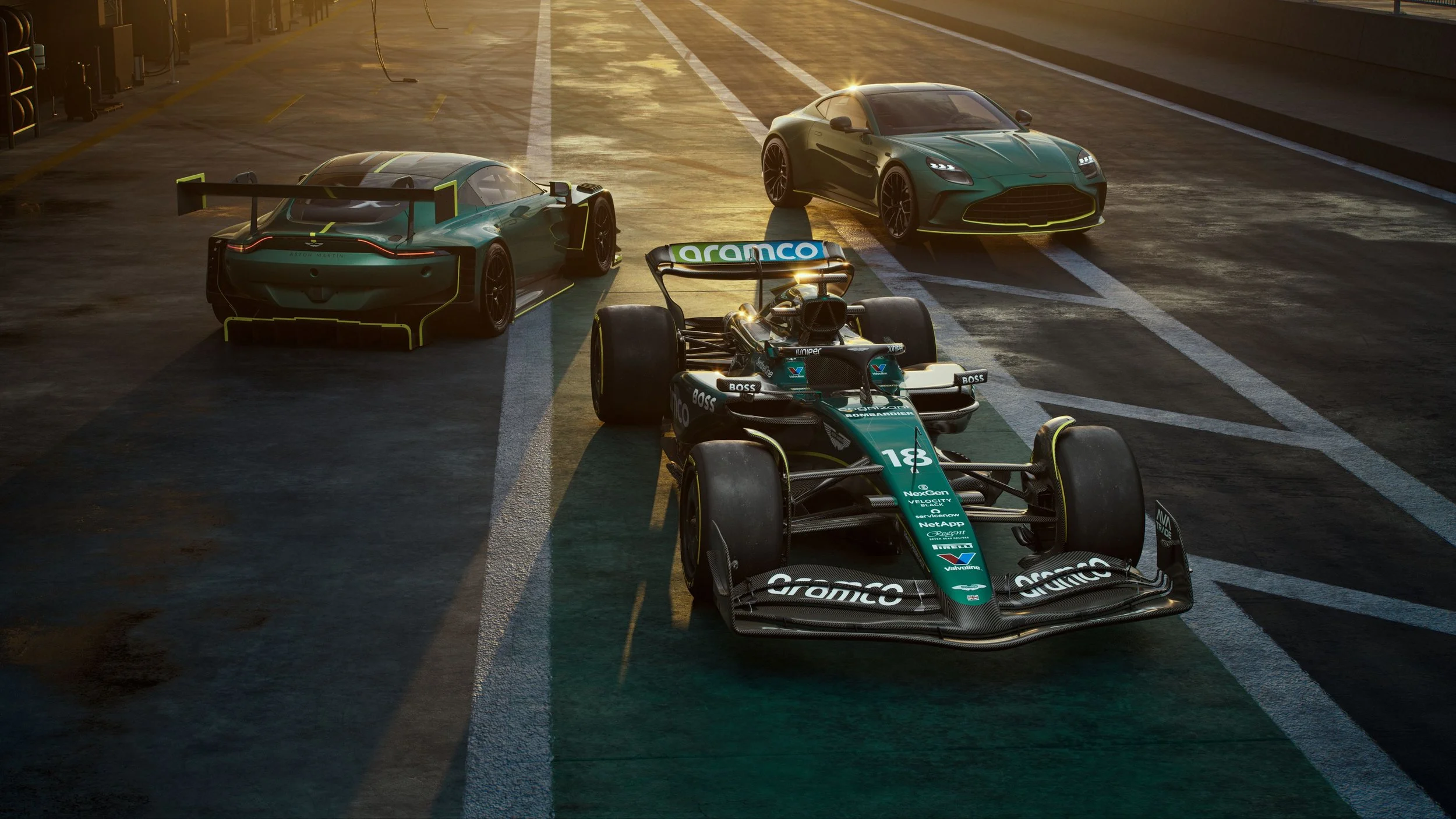 Three race cars inside a garage, with two high-performance cars and one open-wheel race car in the foreground, illuminated by warm lighting.
