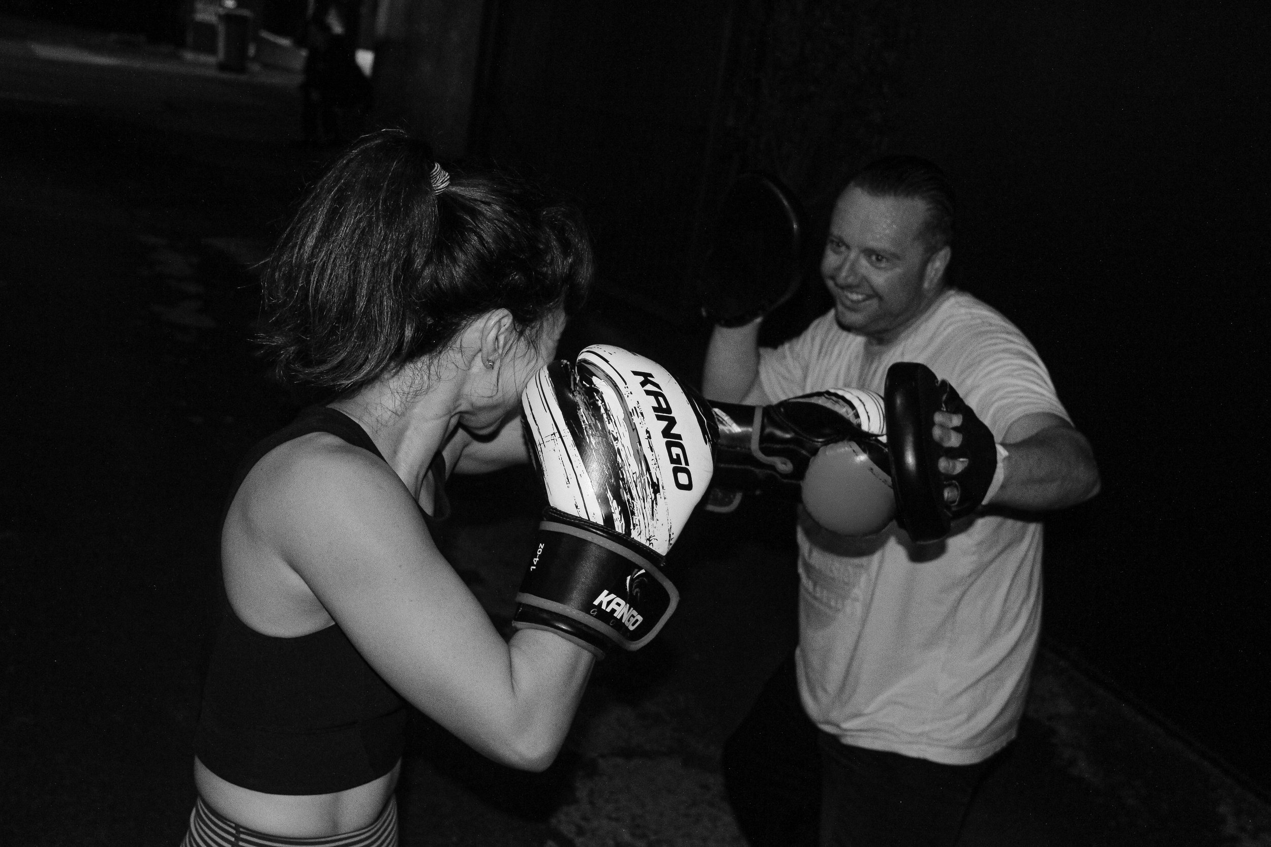 Woman boxing outdoors with a trainer holding focus mitts