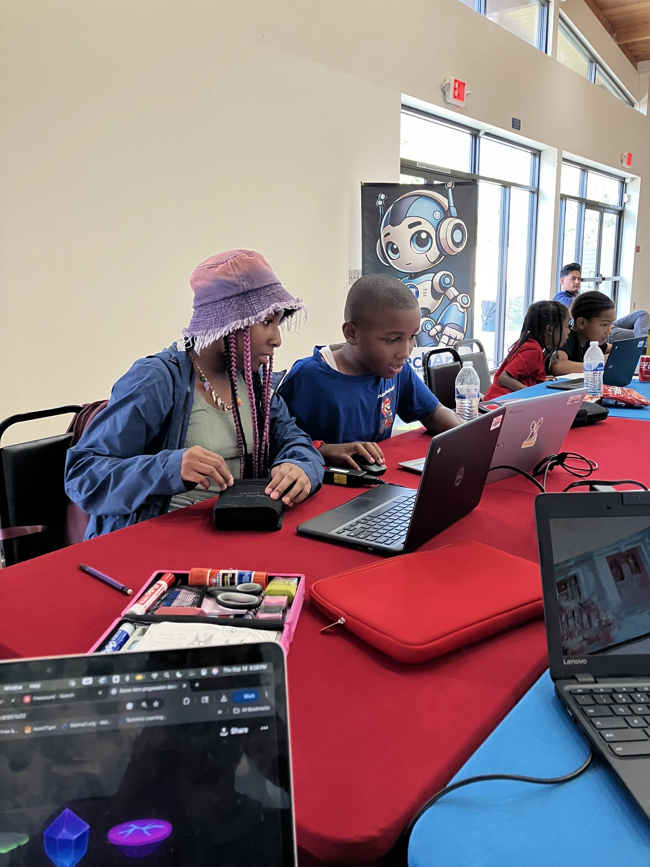 Child using a tablet with colorful programming blocks on the screen, surrounded by red, yellow, and green cube-shaped toys on a white surface.