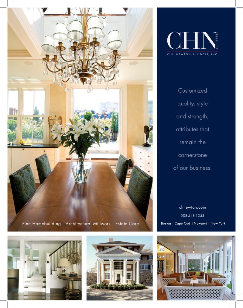 Interior view of a dining room with a wooden table, a vase of white lilies, a chandelier, and large windows with a cityscape in the background.