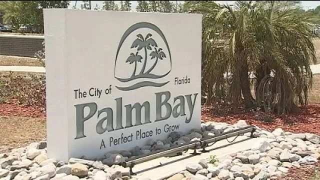 Sign for the city of Palm Bay, Florida with the slogan 'A Perfect Place to Grow', featuring palm trees and an illustration of the sun.