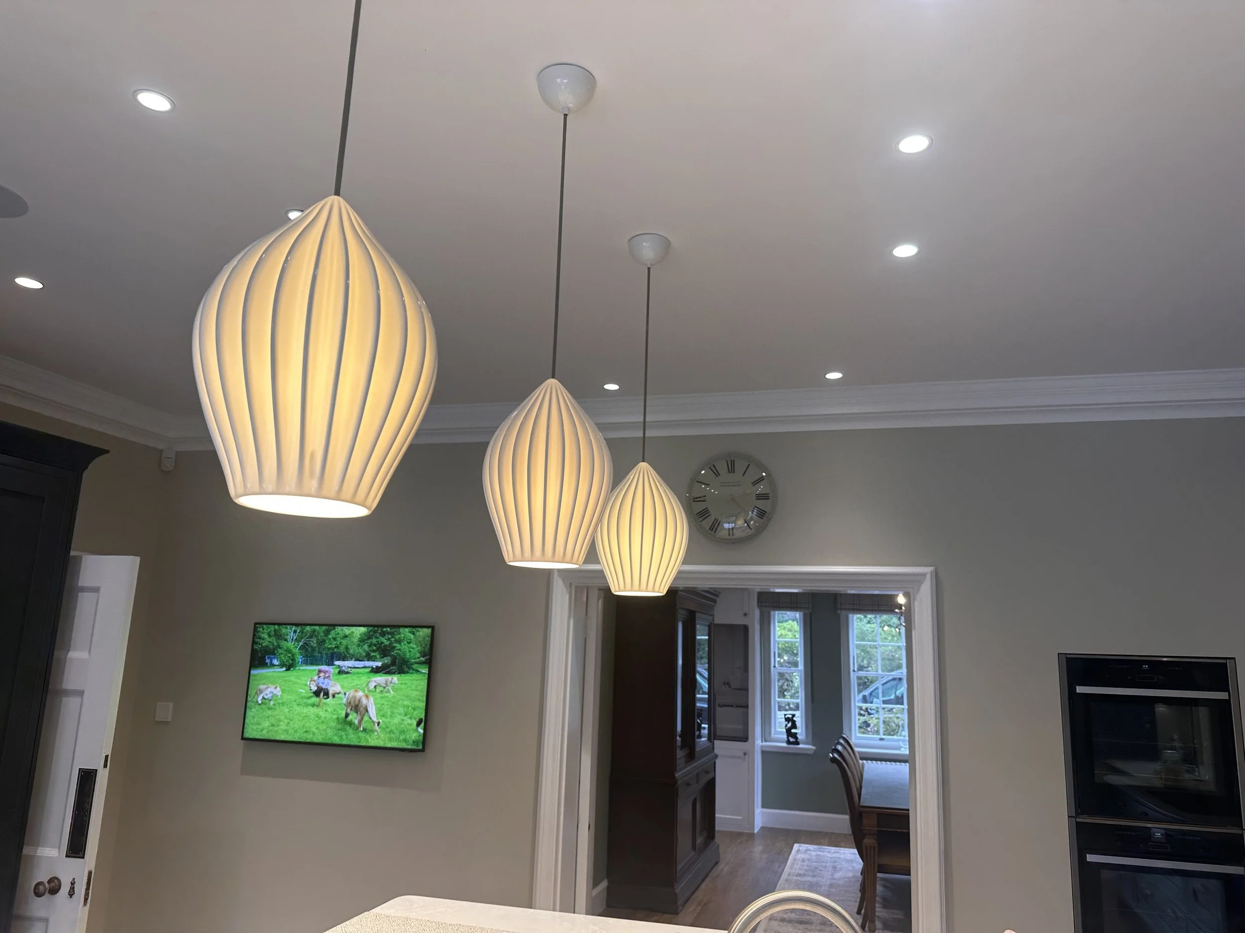 Kitchen with pendant lights, wall clock, TV displaying a meadow scene, open doorway to dining area.