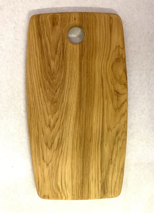 A rectangular wooden cutting board with rounded edges and a hole at the top for hanging, placed on a white surface.