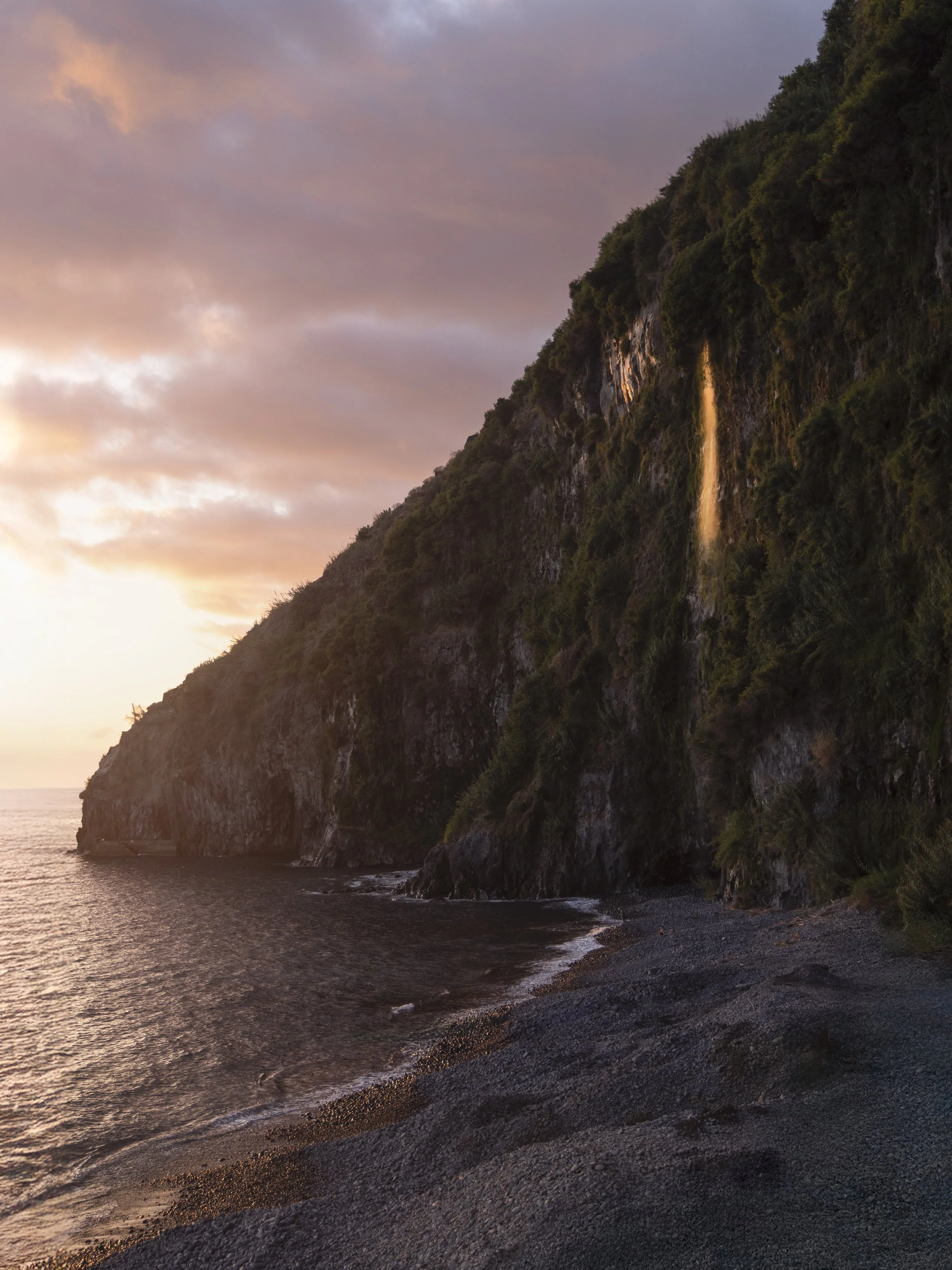The setting sun illuminates a cliffside waterfall on the southern coast of Madeira, Portugal.