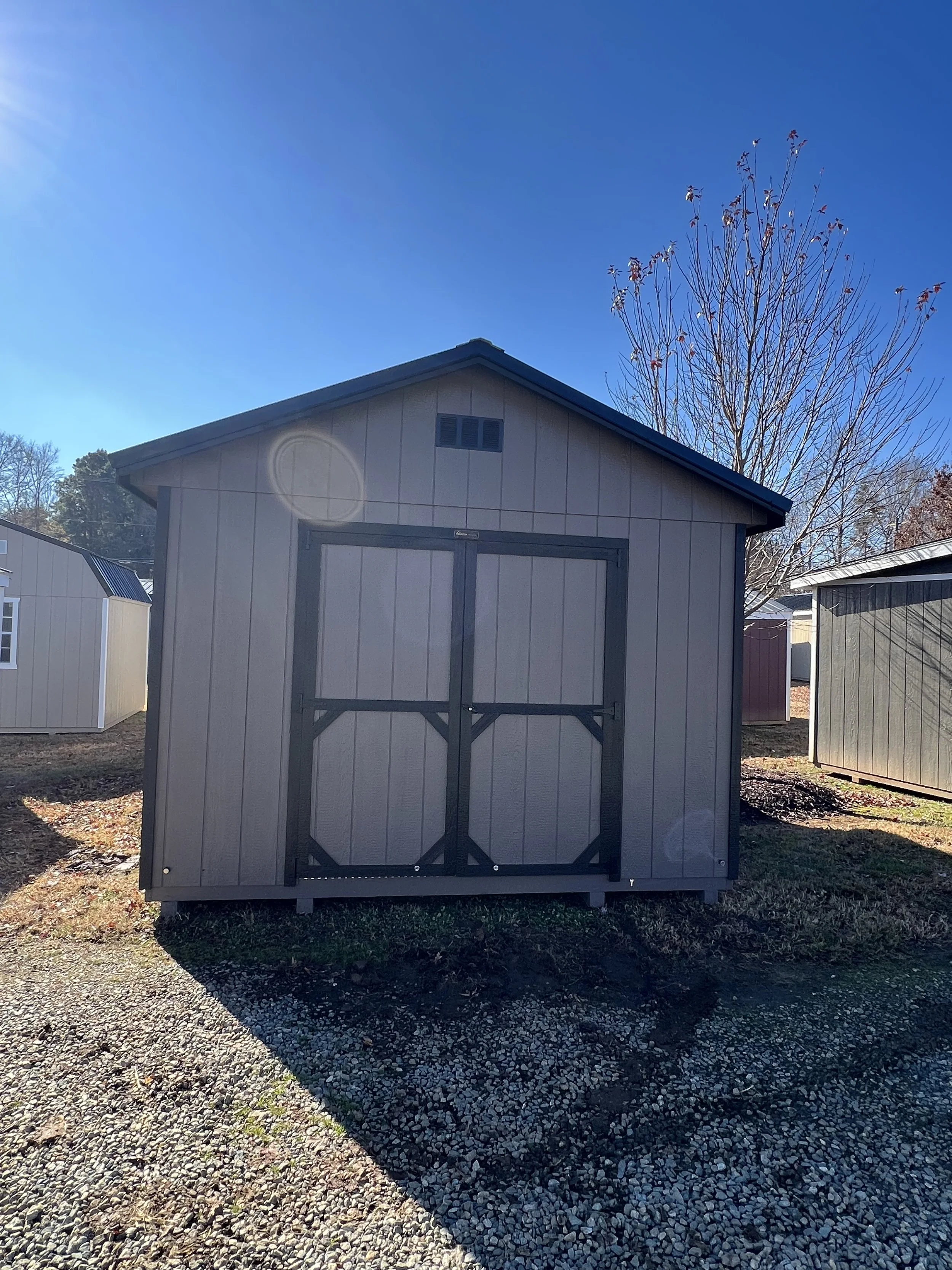 A burnished slate deluxe shed with dark trim and a metal roof, situated on green grass under a clear blue sky.